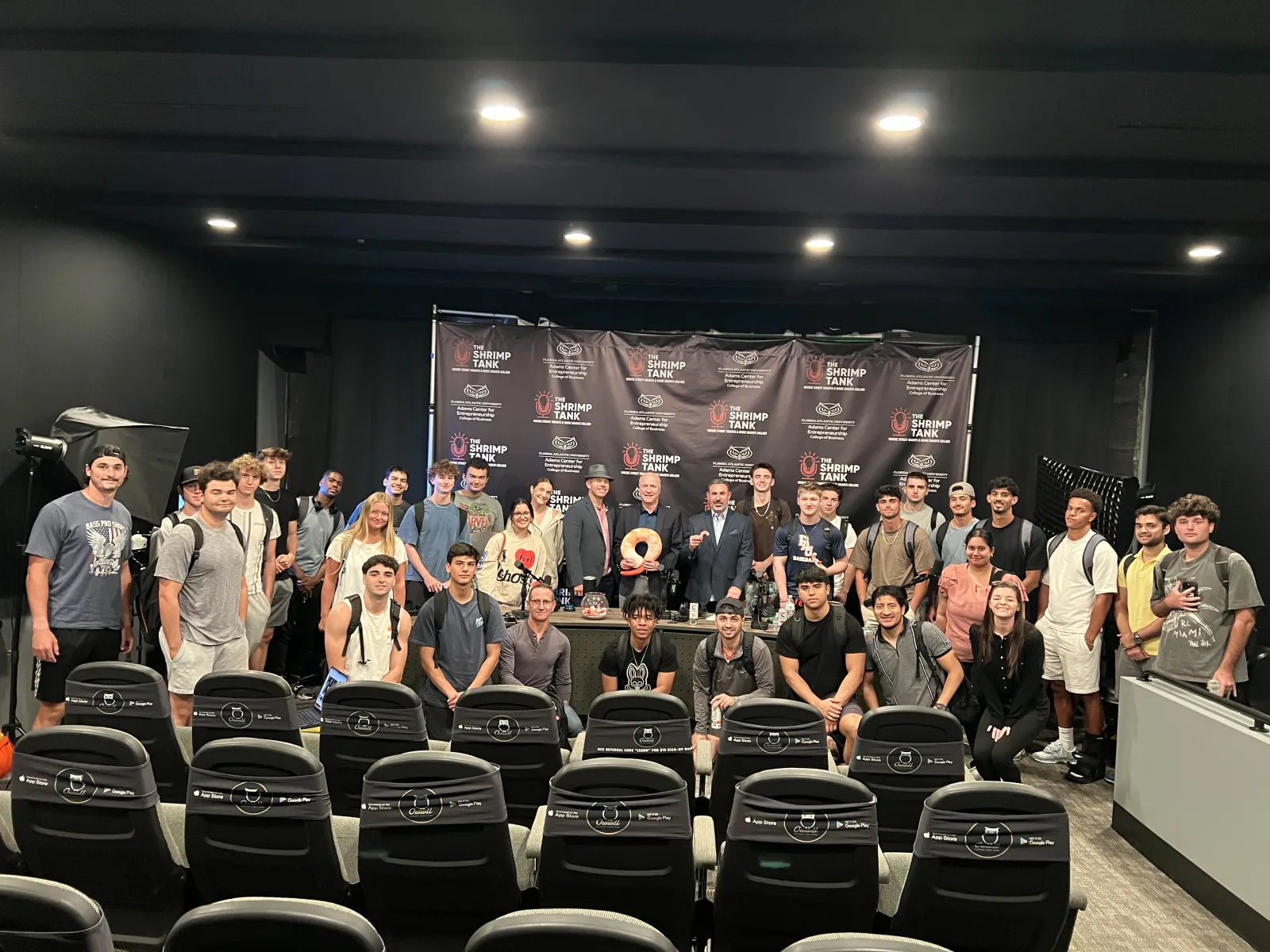 Group photo of diverse young adults and professionals gathered in front of a Shrimp Tank event backdrop in a studio.