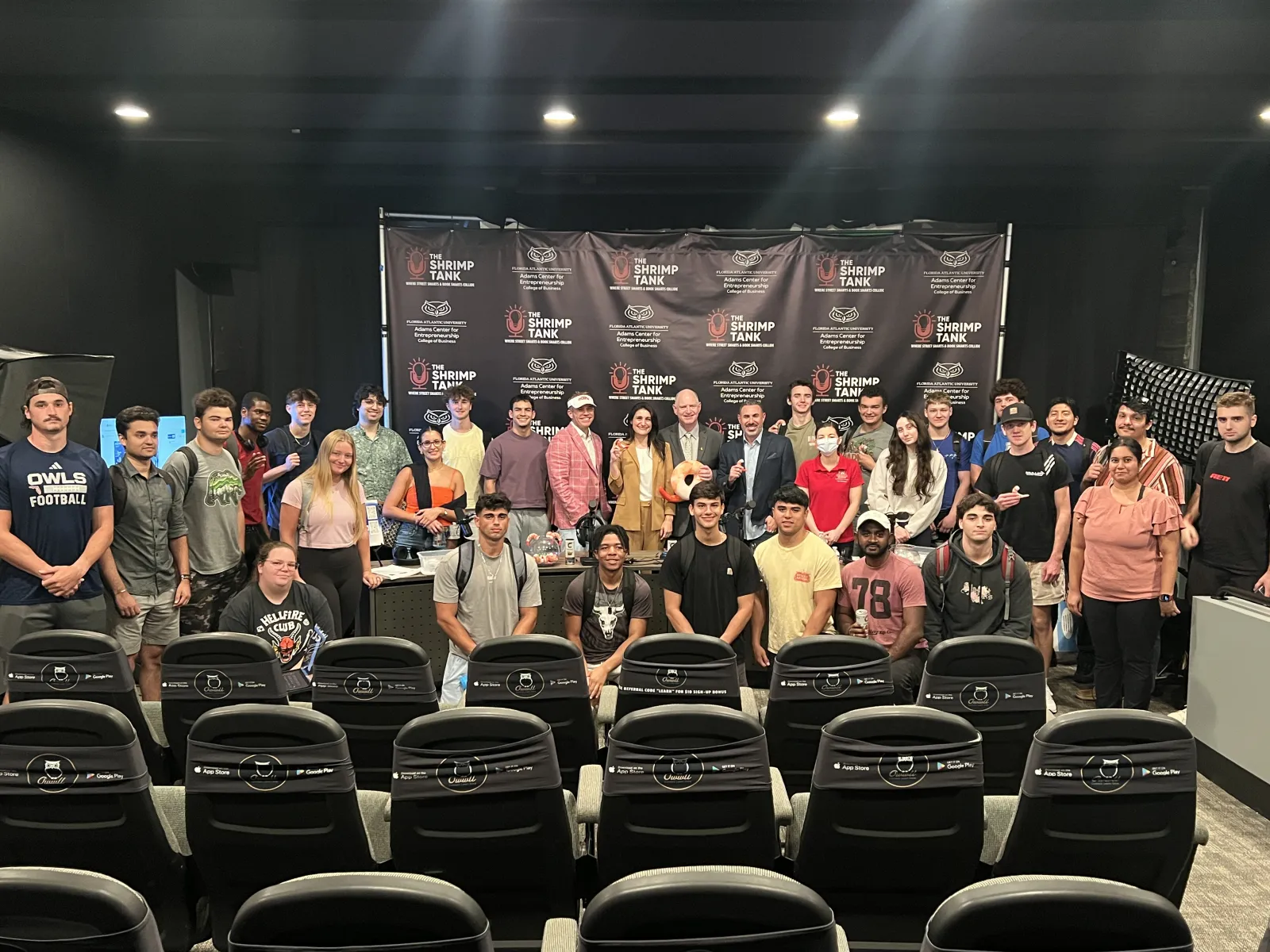 Group of diverse young adults and instructors posing in front of a Shrimp Tank event backdrop in a conference room.