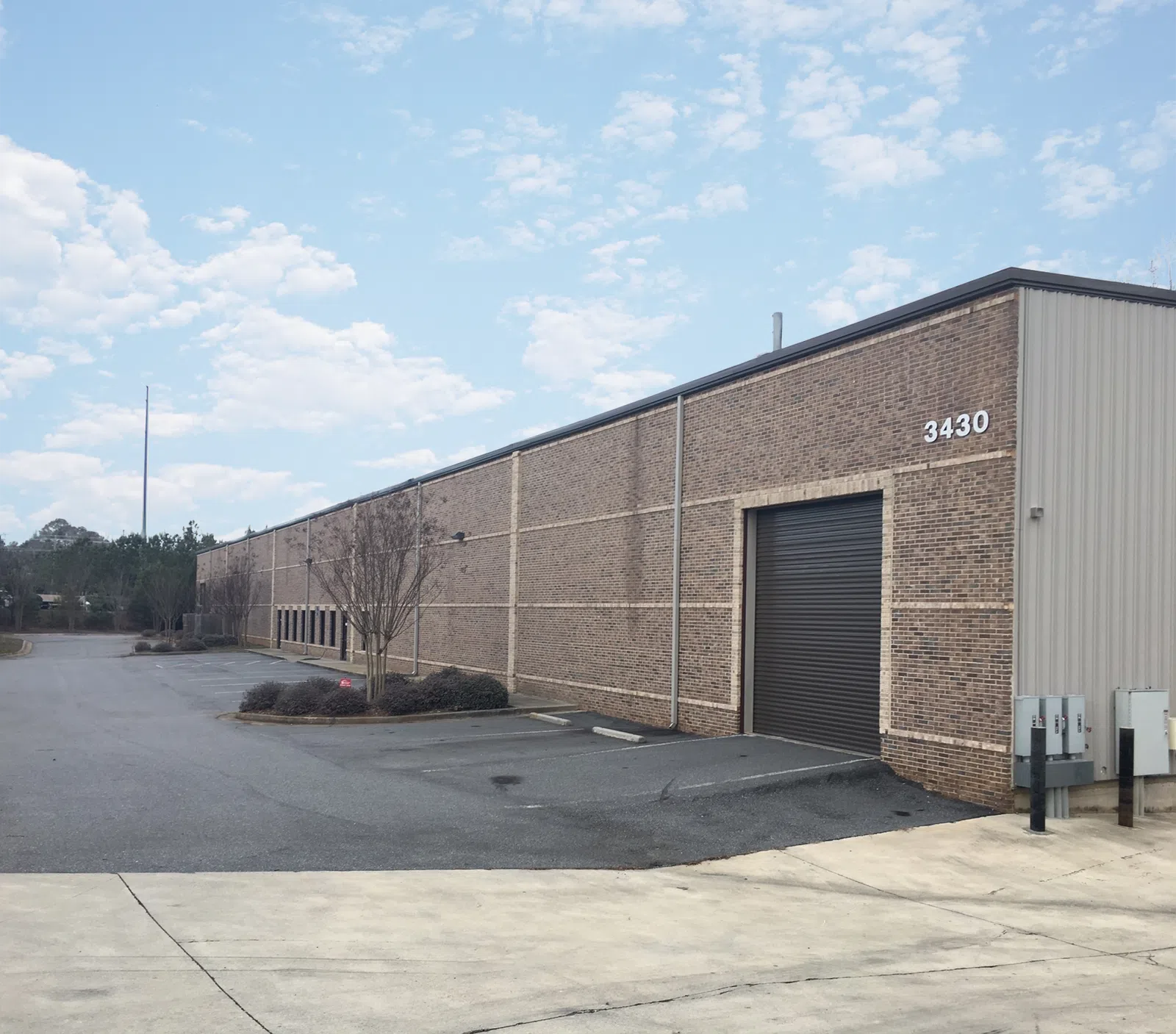 Long brick warehouse building with large black rolling door and address number 3430 on side, clear sky background.