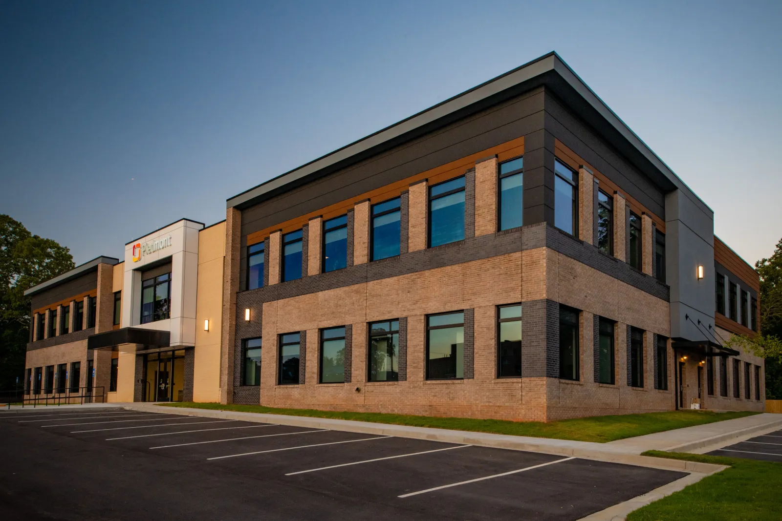 Modern two-story office building with large windows and brick exterior during early evening with empty parking lot.