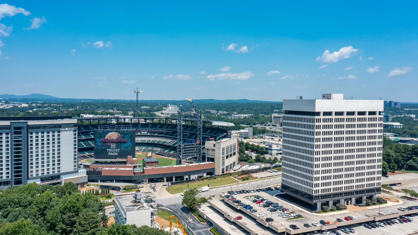 Aerial view of Truist Park baseball stadium with surrounding buildings and parking lots under blue sky.
