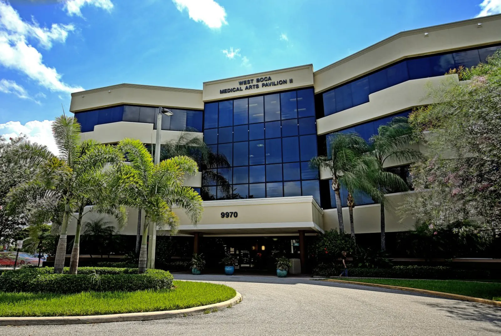 Modern three-story medical office building with palm trees and blue sky at West Boca Medical Arts Pavilion