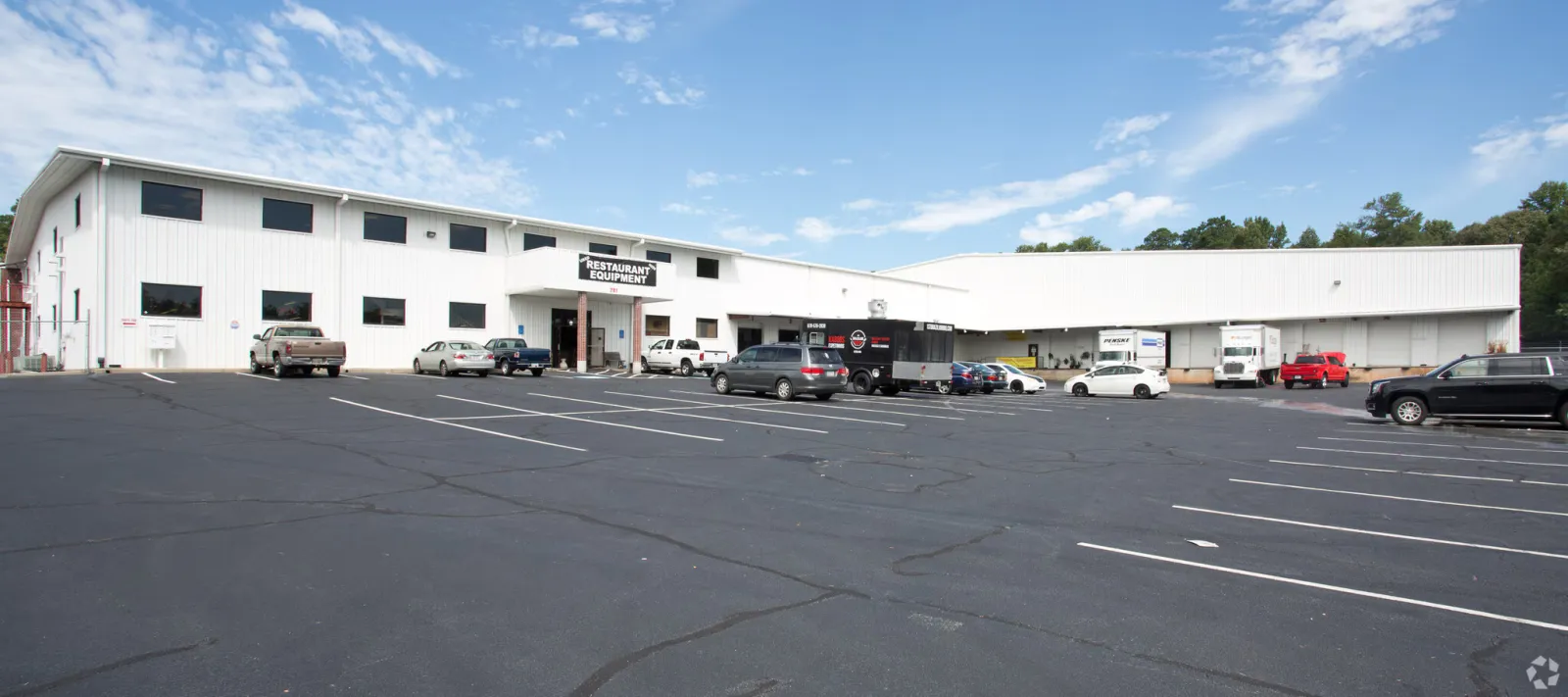 Large white commercial building with restaurant equipment sign and parked vehicles under blue sky.