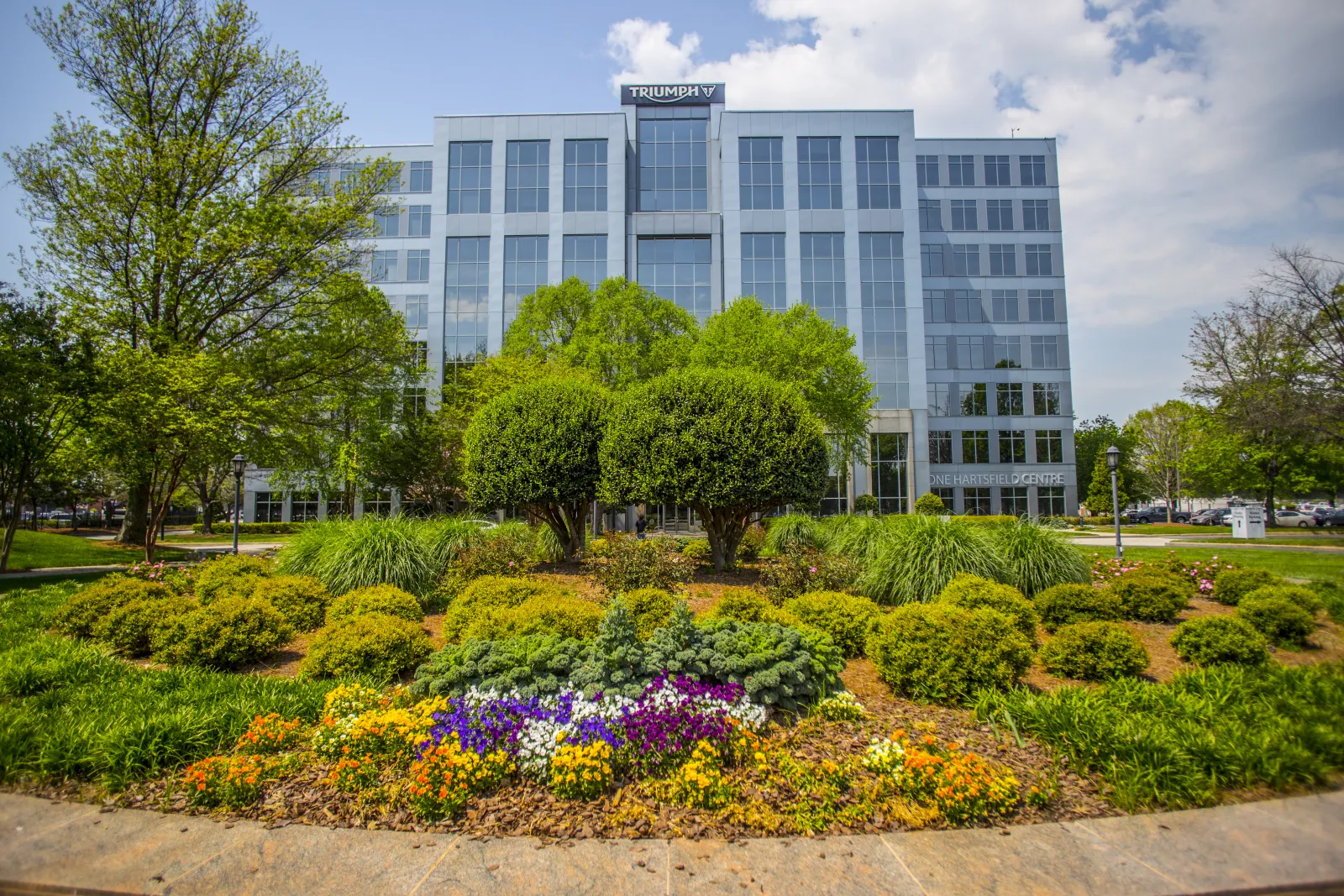 Modern glass office building behind a landscaped garden with colorful flowers and green shrubs under a blue sky