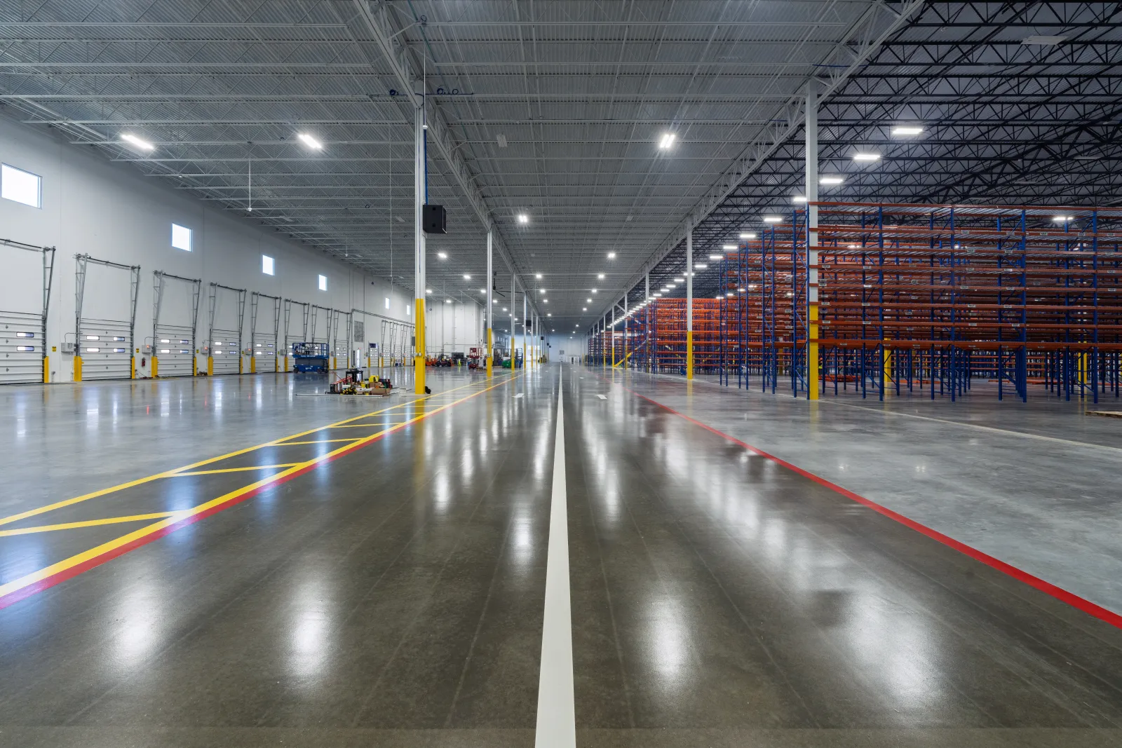 Spacious industrial warehouse with empty shelving units and polished concrete floors under bright LED lighting.
