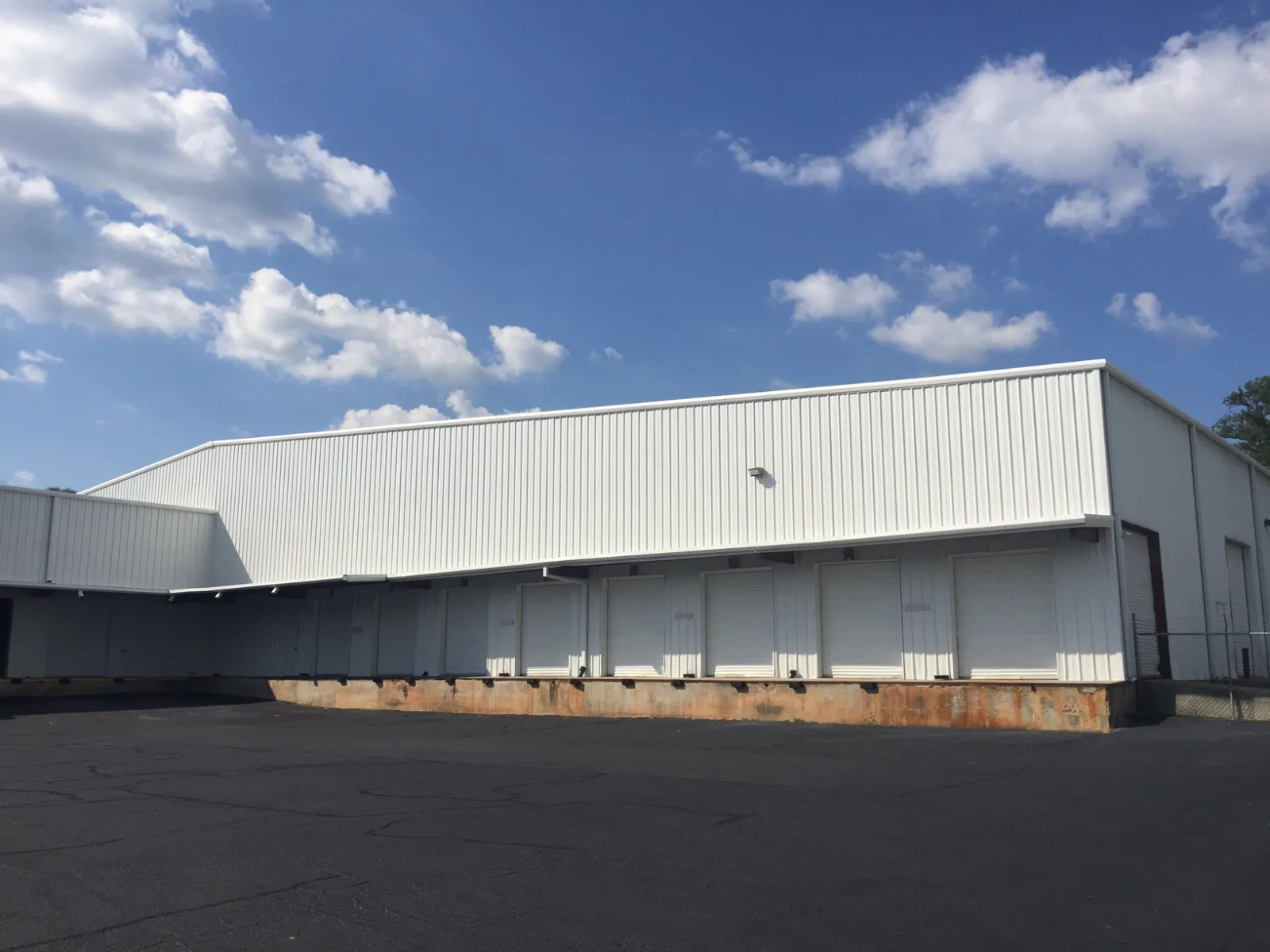 White industrial warehouse with multiple loading dock doors under a partly cloudy blue sky.