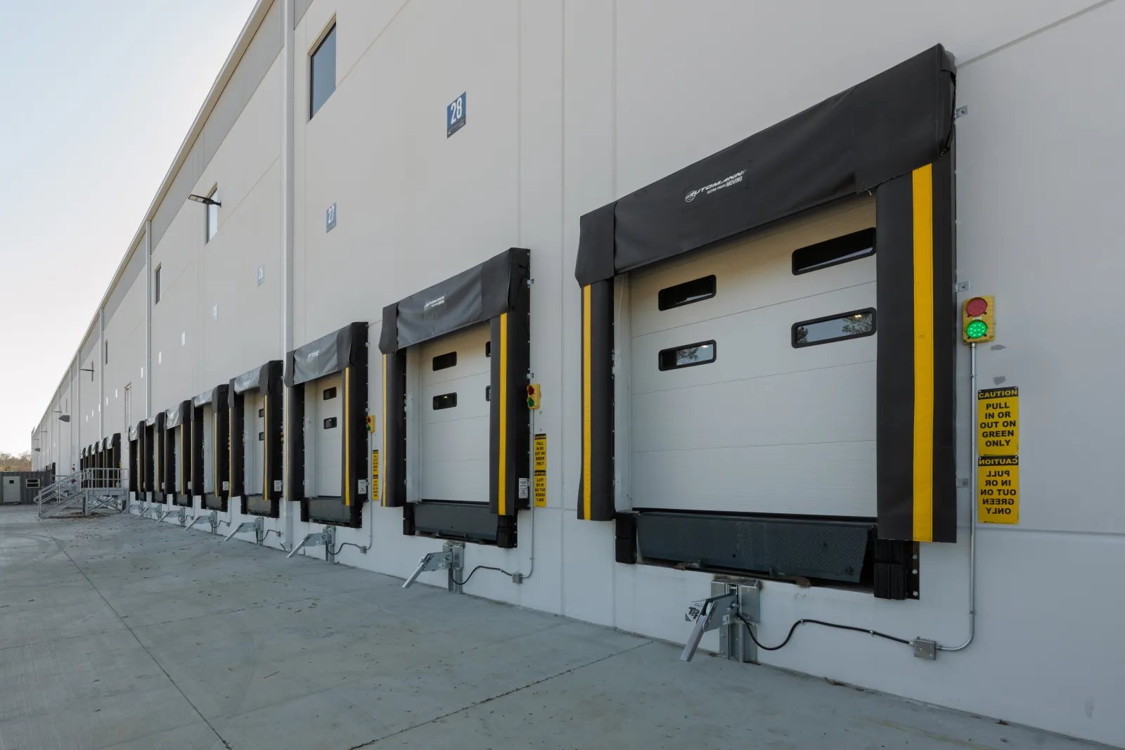 Row of modern loading dock doors with protective seals on industrial warehouse exterior under clear sky.