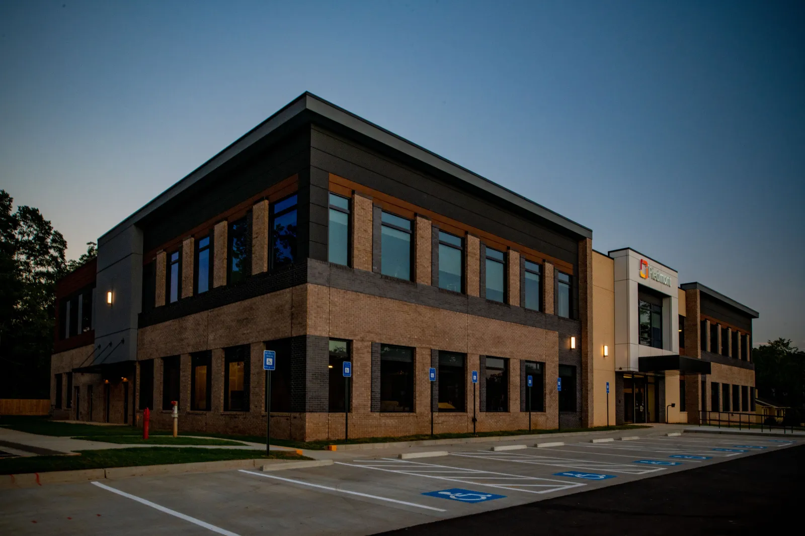 Modern two-story office building with brick and glass exterior at dusk with empty handicap parking spaces