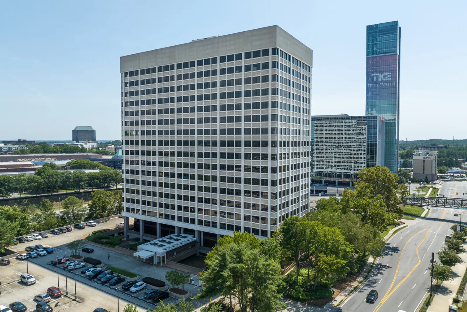 Modern office building with large windows surrounded by trees and parking lots under clear blue sky