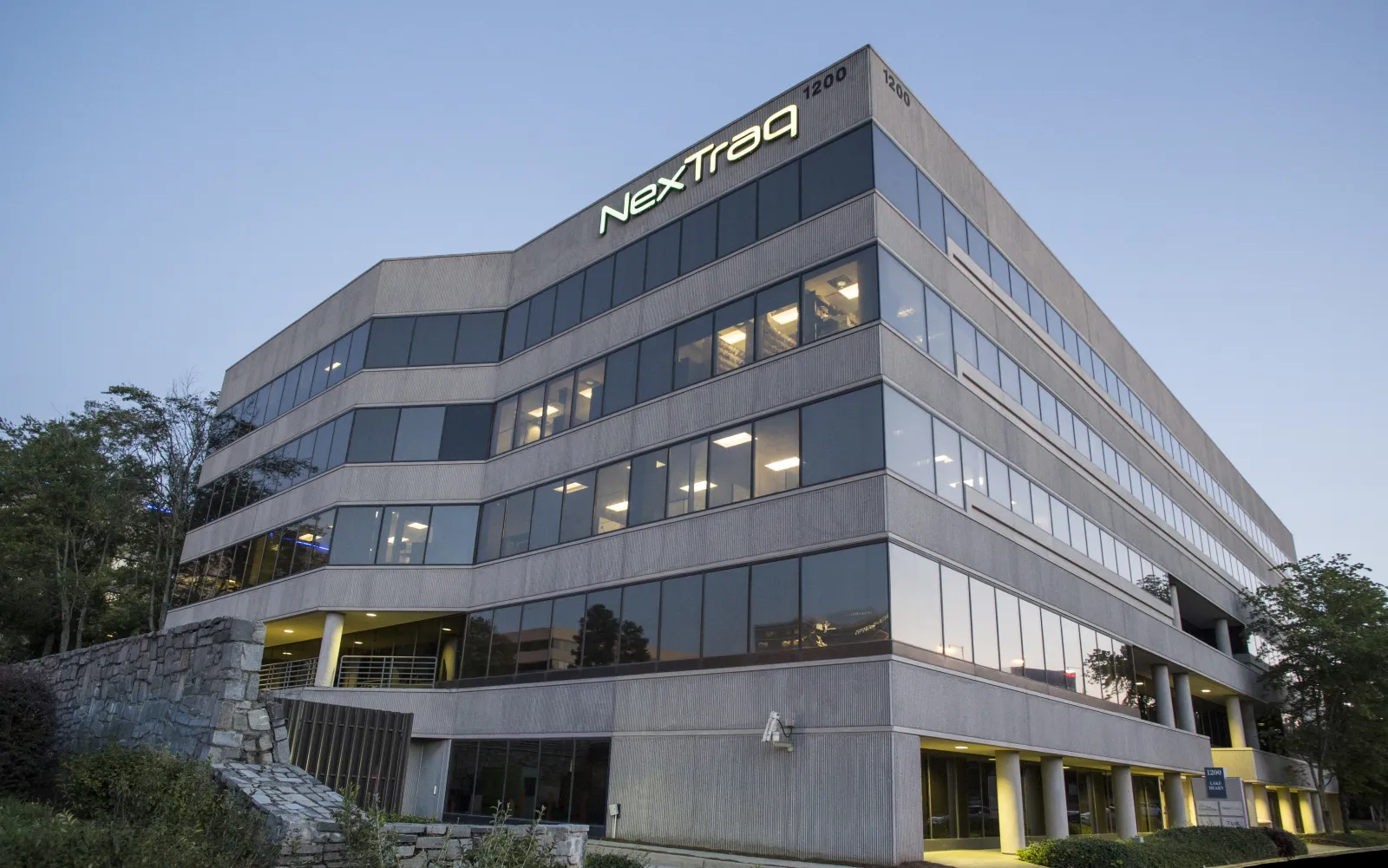 Modern office building of NexTraq with illuminated logo at the top corner during early evening.