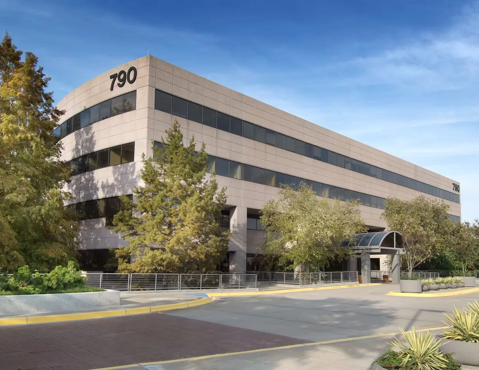 Modern office building with large windows, trees, and clear blue sky at 790 address.