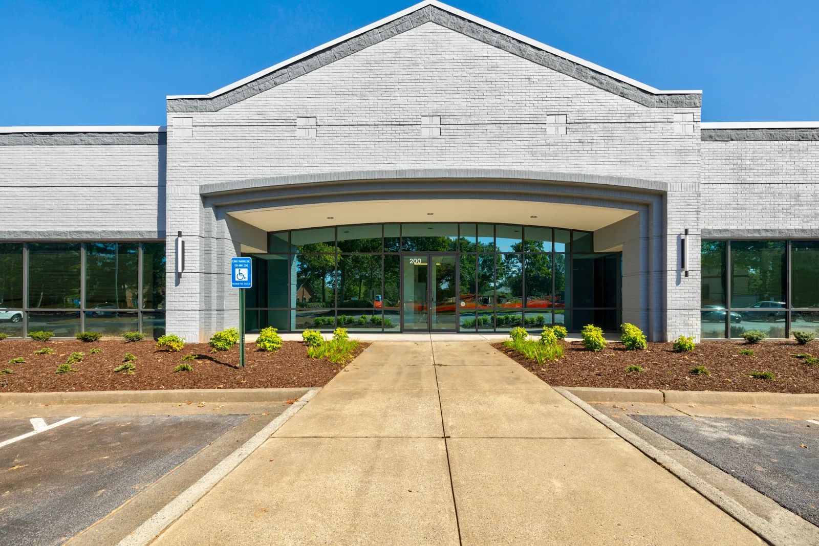 Modern commercial building front with wide entrance, large windows, and clear blue sky.