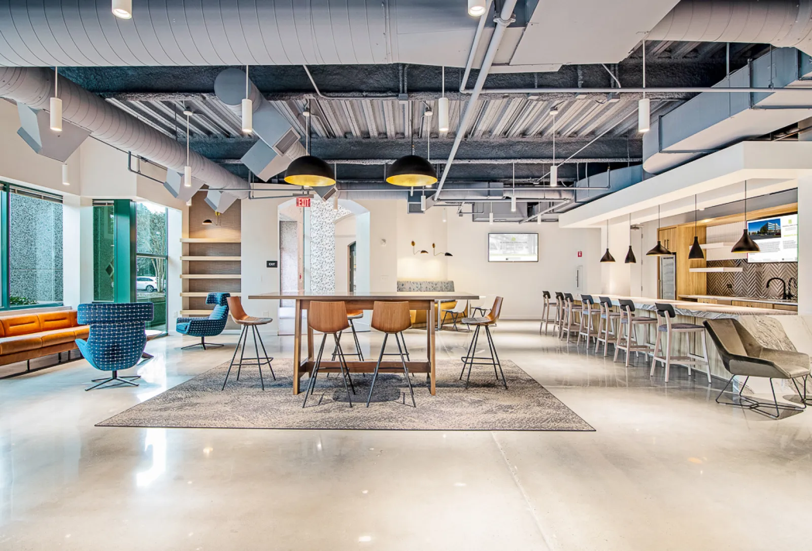 Modern office lounge with a long table, bar stools, comfortable seating, and industrial ceiling design
