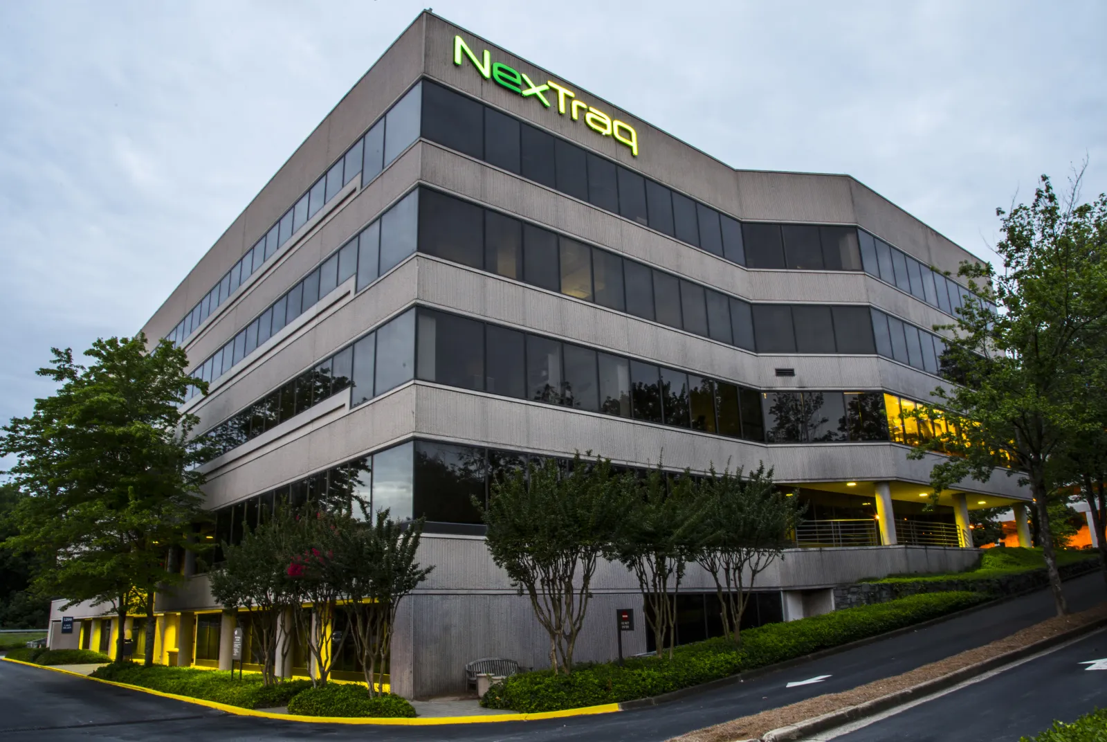 Modern office building with NexTraq logo on top, surrounded by trees and greenery under a cloudy sky