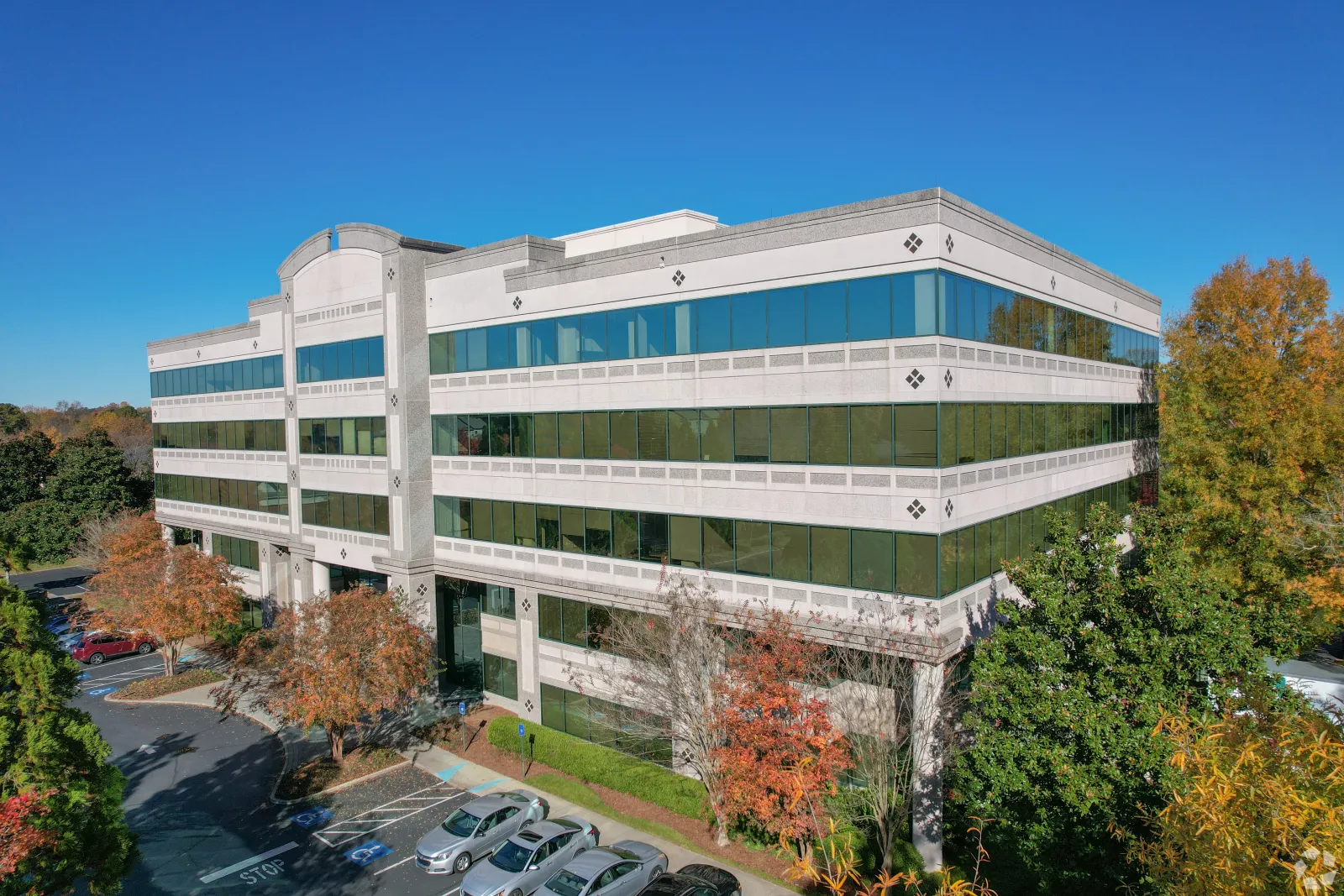 Modern office building with large glass windows surrounded by trees and parked cars under a clear blue sky