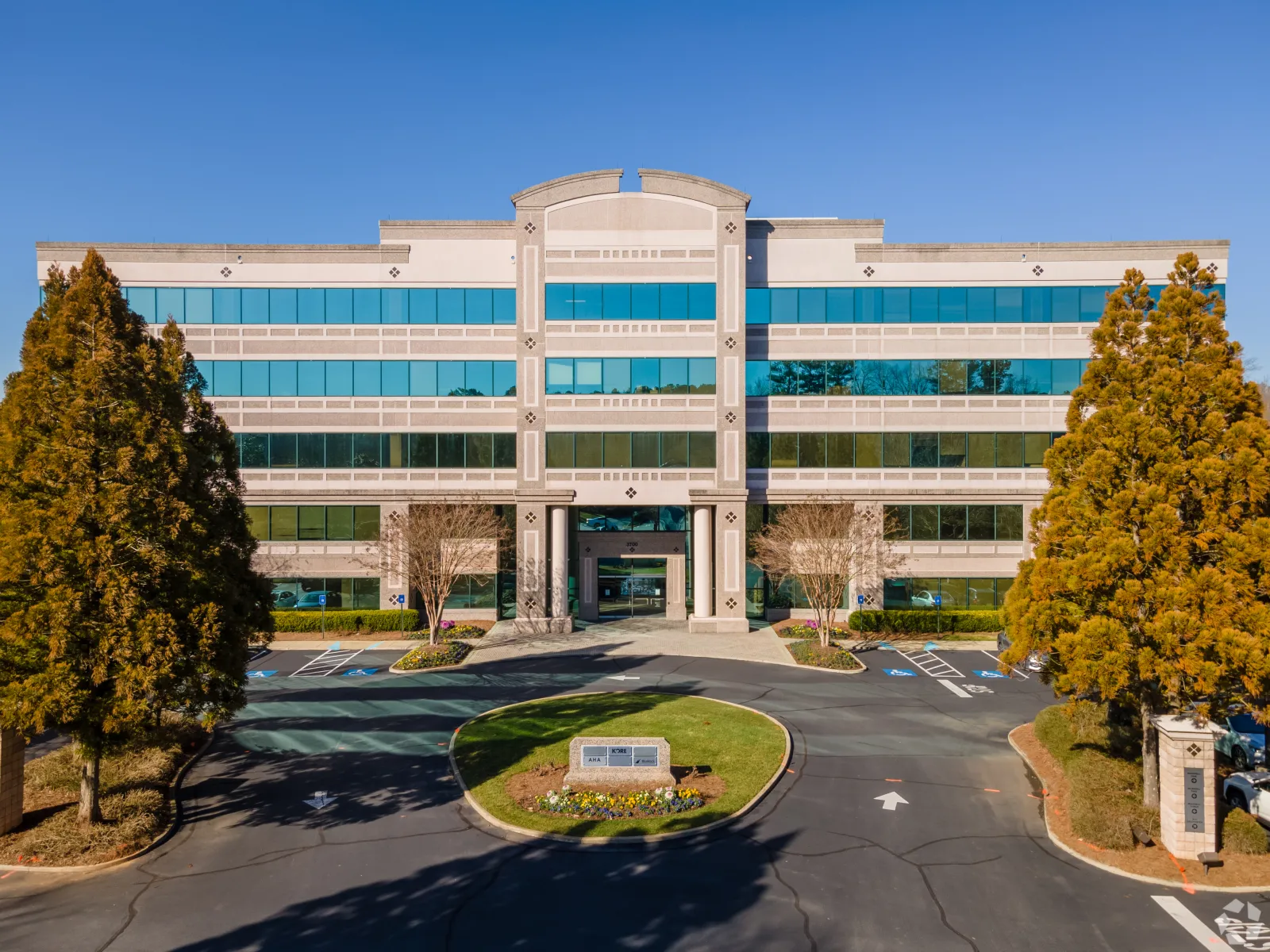 Modern four-story office building with reflective windows, surrounded by trees under a clear blue sky.