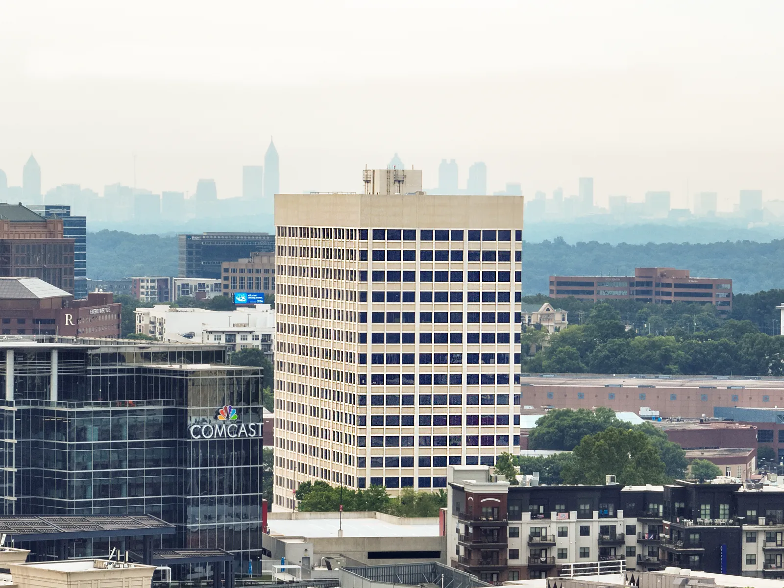 Urban skyline with Comcast building, modern offices, and distant cityscape under a hazy sky.