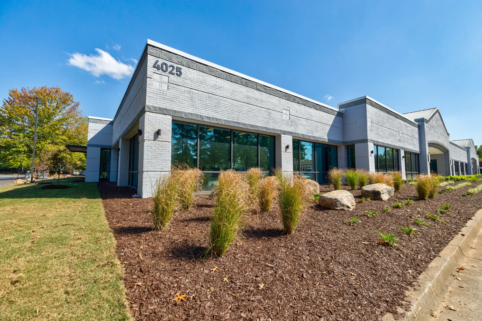 Modern single-story office building with large windows, landscaped garden, and clear blue sky at 4025 address.