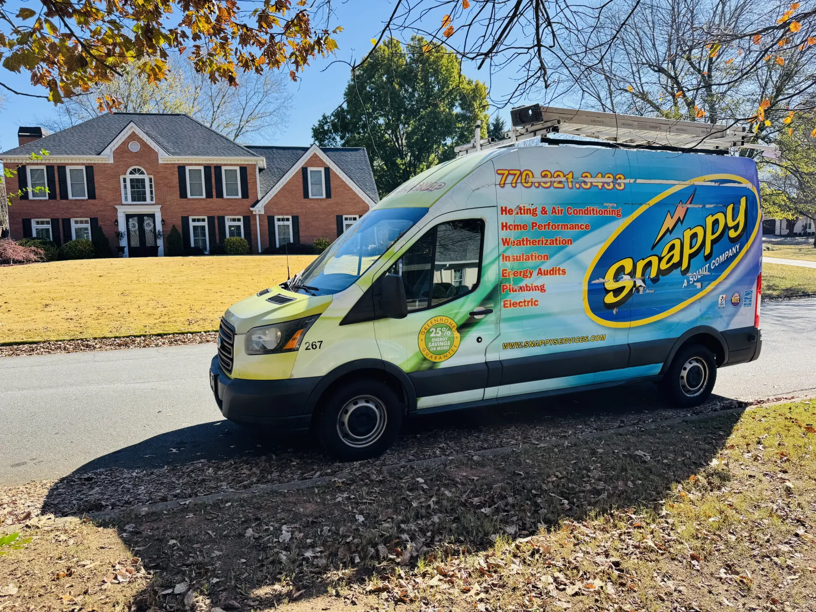 Snappy HVAC service van parked on street in front of suburban brick house with autumn leaves on ground.
