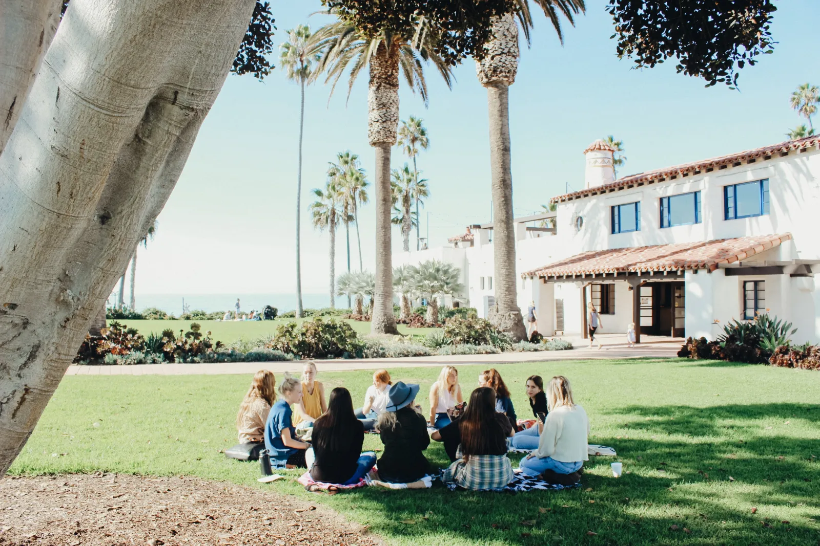 a group of women sitting on the grass in front of a building