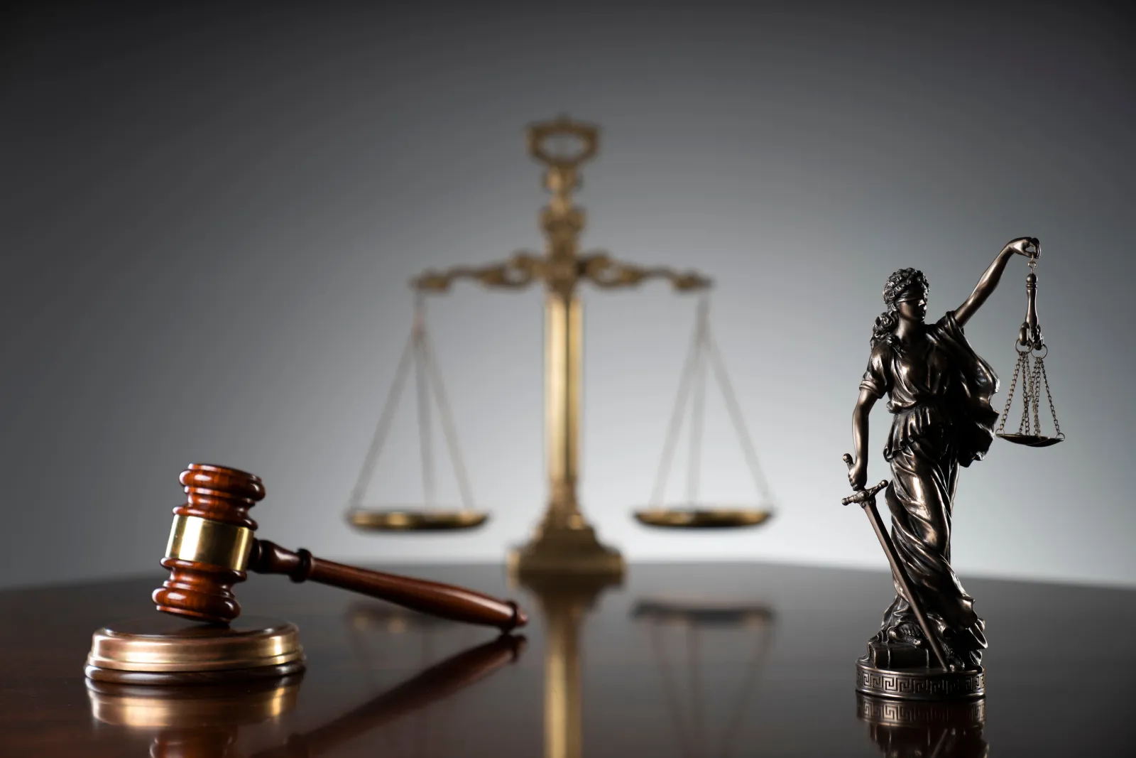 A wooden gavel and golden scales of justice on a desk.