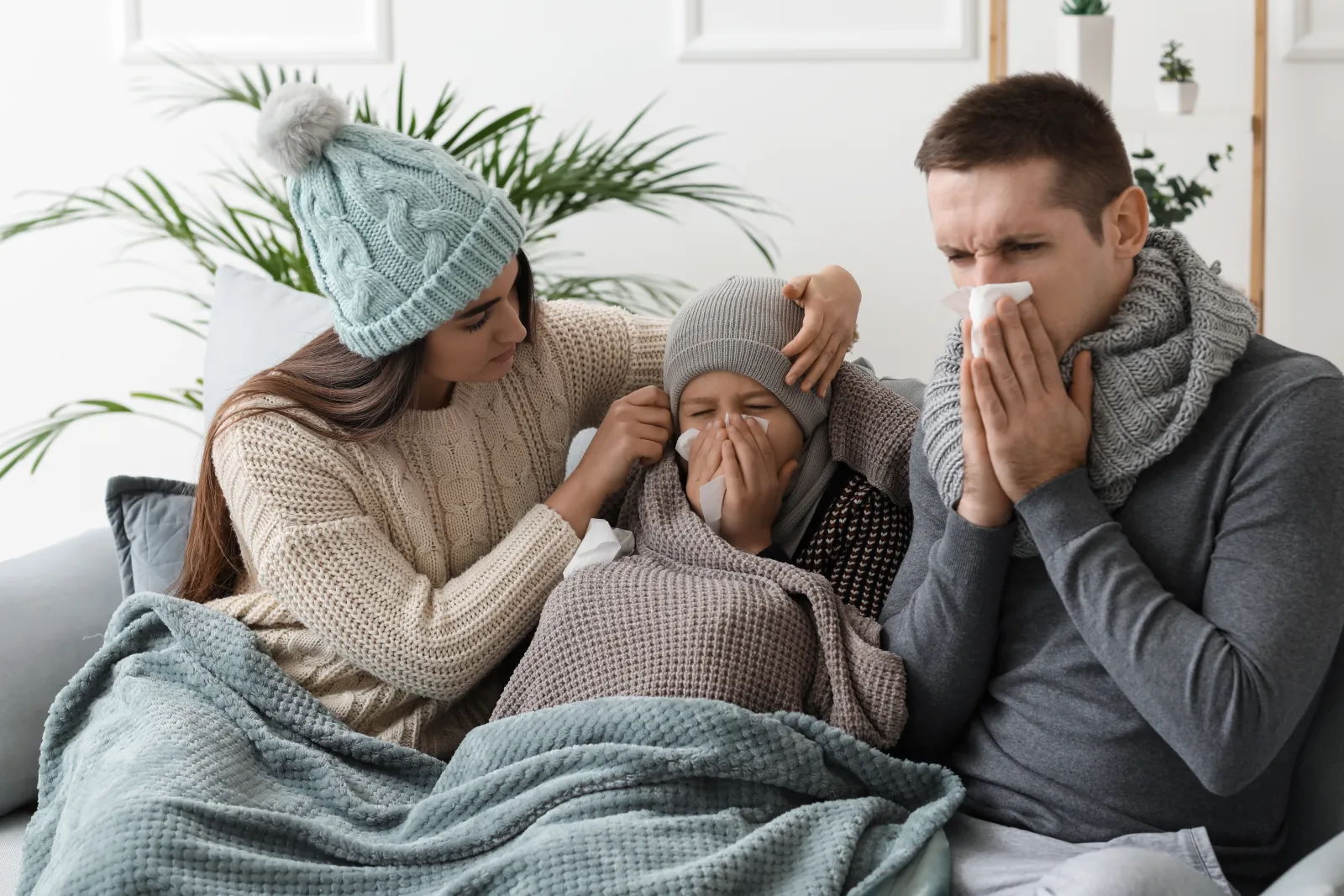 Family with the flu bundles up on the couch with sweaters and blankets