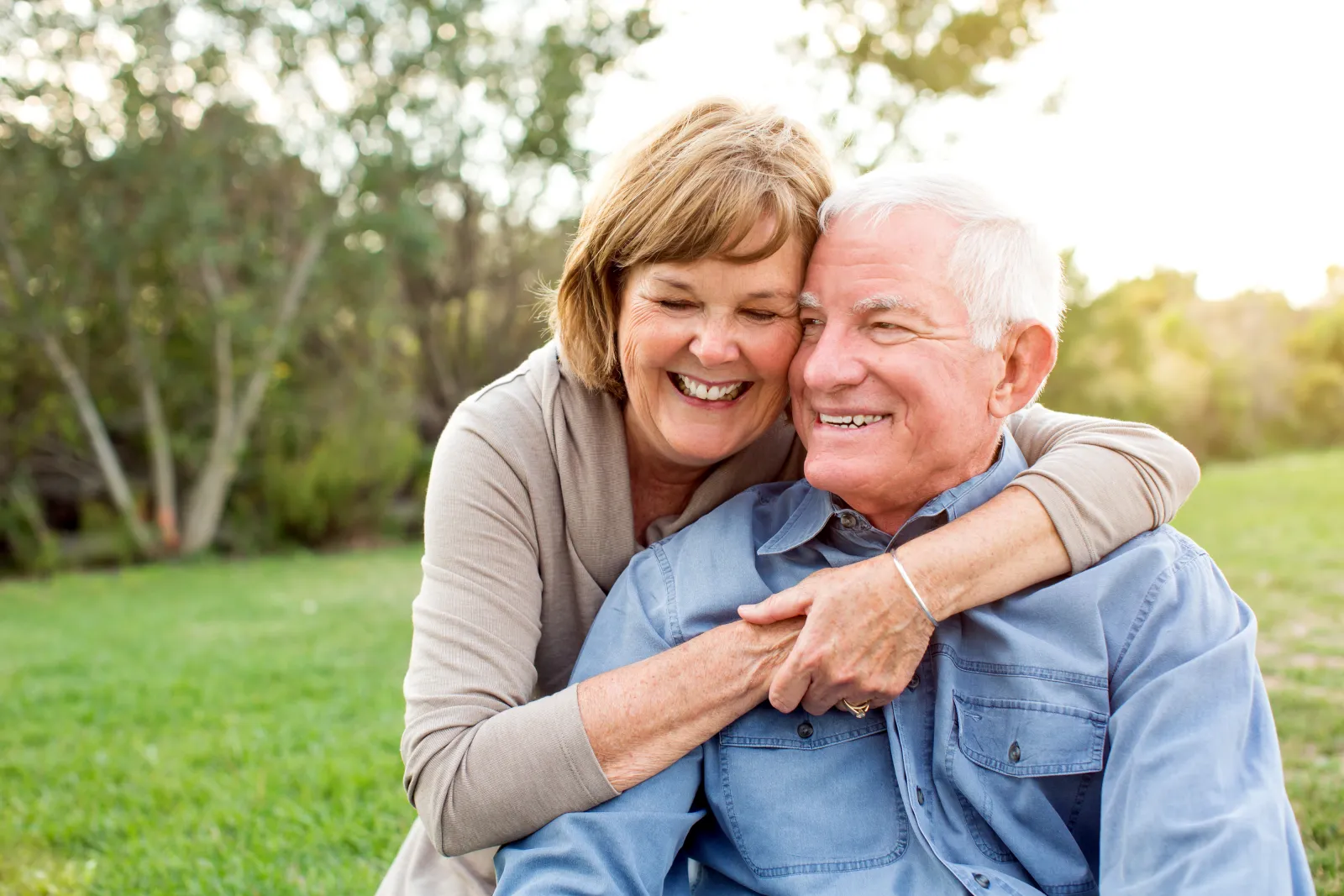 Smiling older woman hugs her husband outdoors after beating cancer