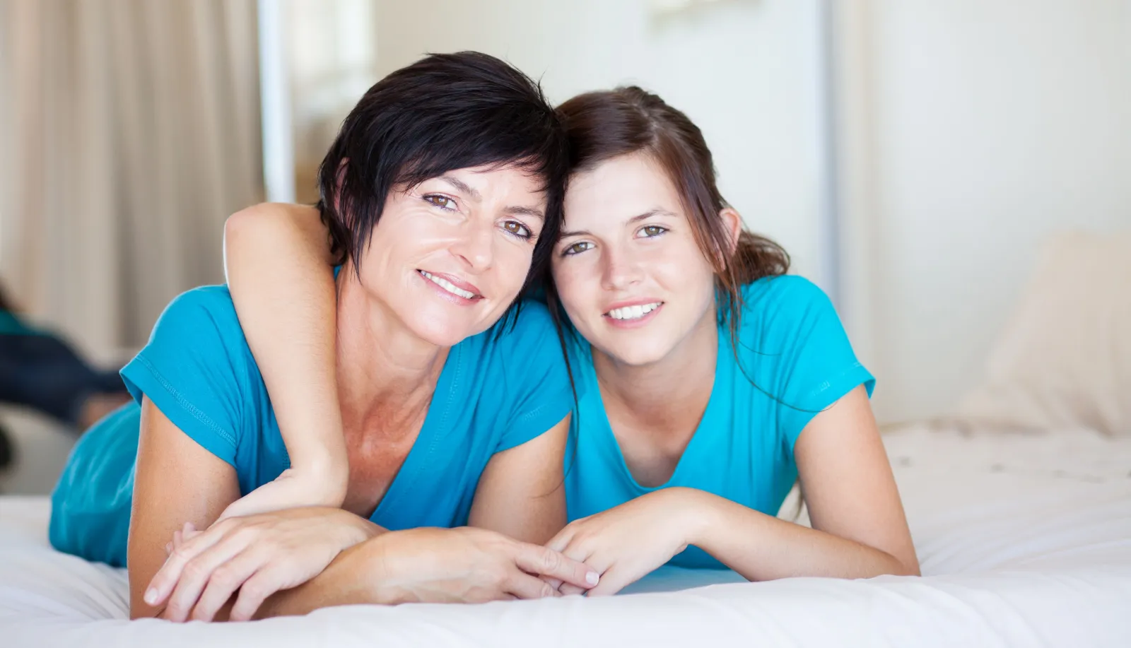 Mother and daughter holding each other posing on top of a bed