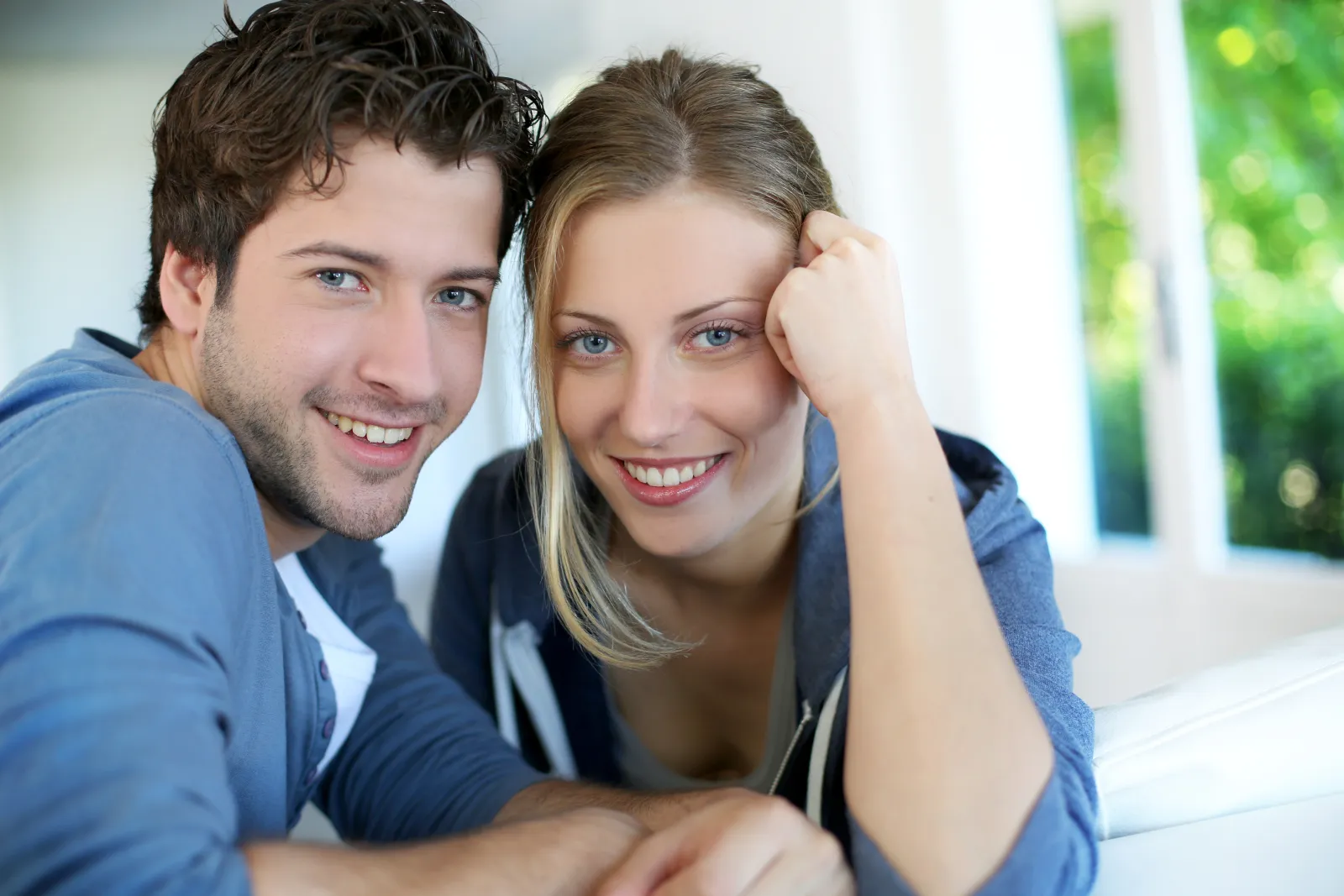 Healthy, smiling couple wearing blue kneeling together in front of their house