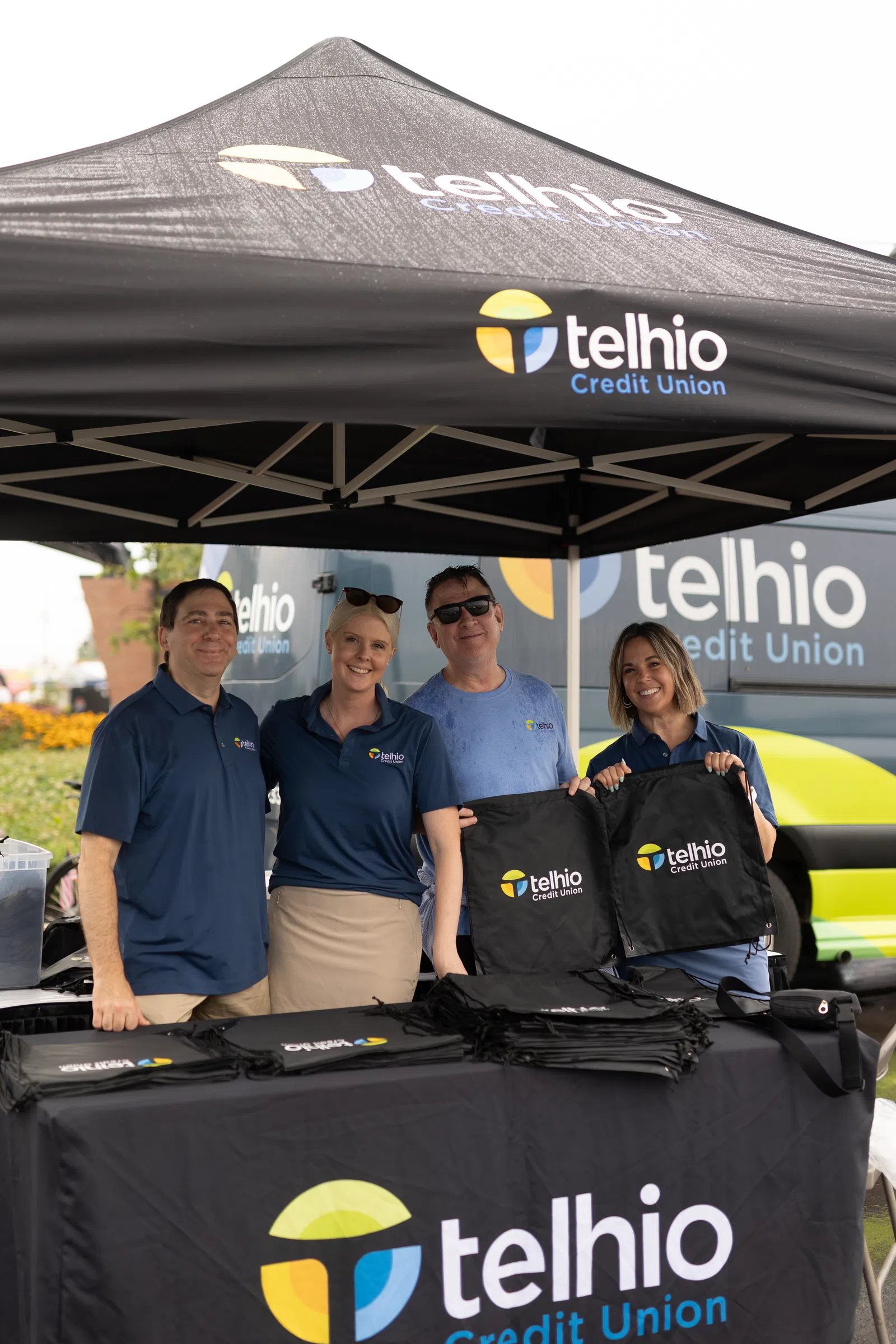 Four smiling staff at a Telhio Credit Union booth with branded tent and giveaways outdoors