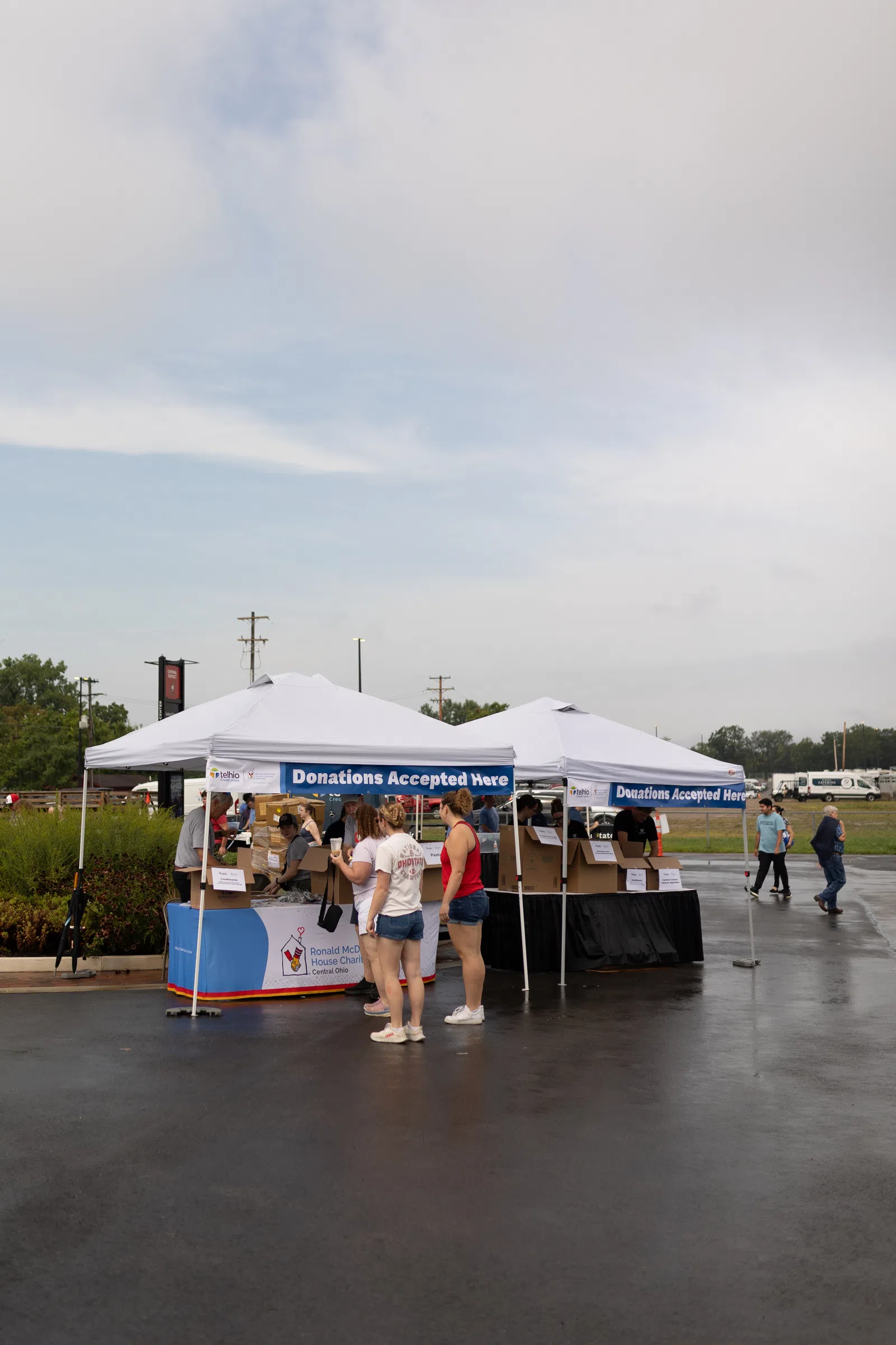 People donating items at outdoor tents with signs reading Donations Accepted Here on a cloudy day.