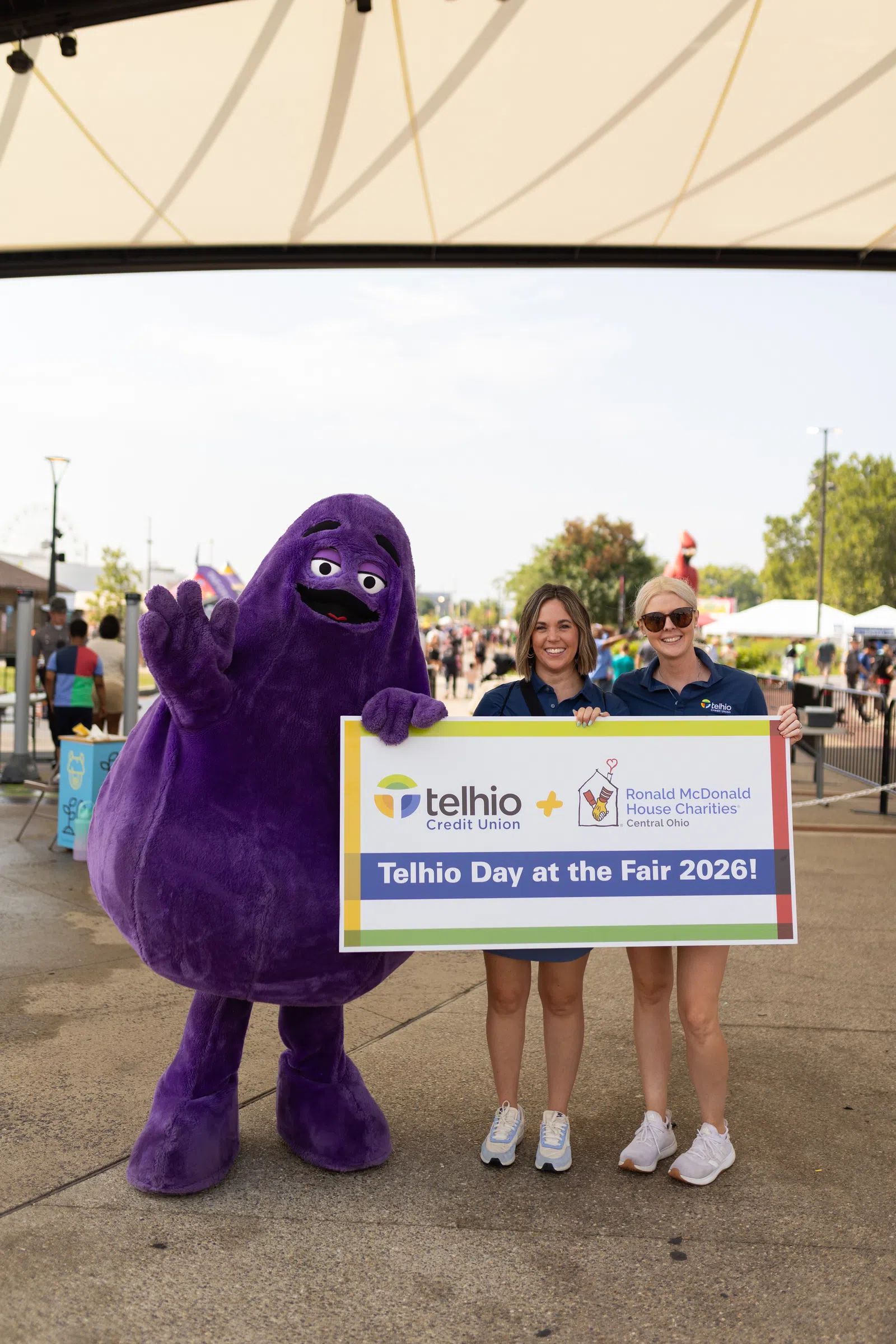 Two women and a purple mascot hold a sign for Telhio Day at the Fair 2026 supporting Ronald McDonald House Charities.