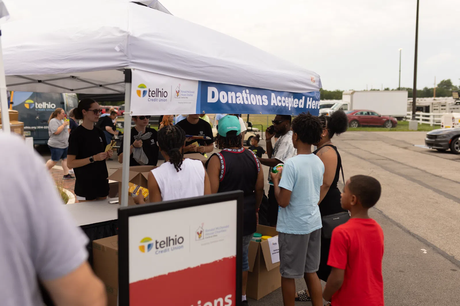 Community members donate goods at a Telhio Credit Union donations booth outdoors under a white tent.