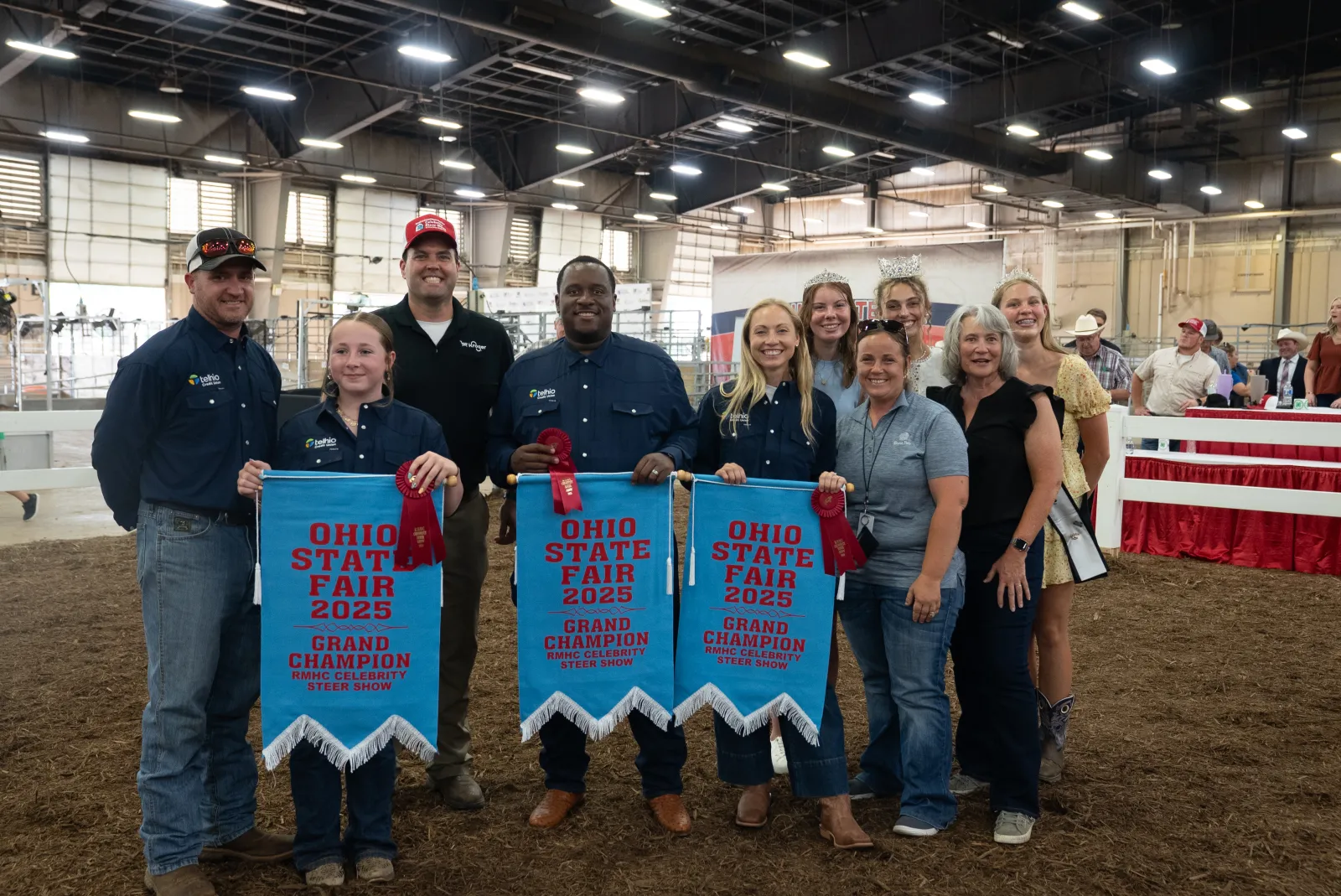 Group of smiling people holding Ohio State Fair 2025 Grand Champion banners inside a fairground building.