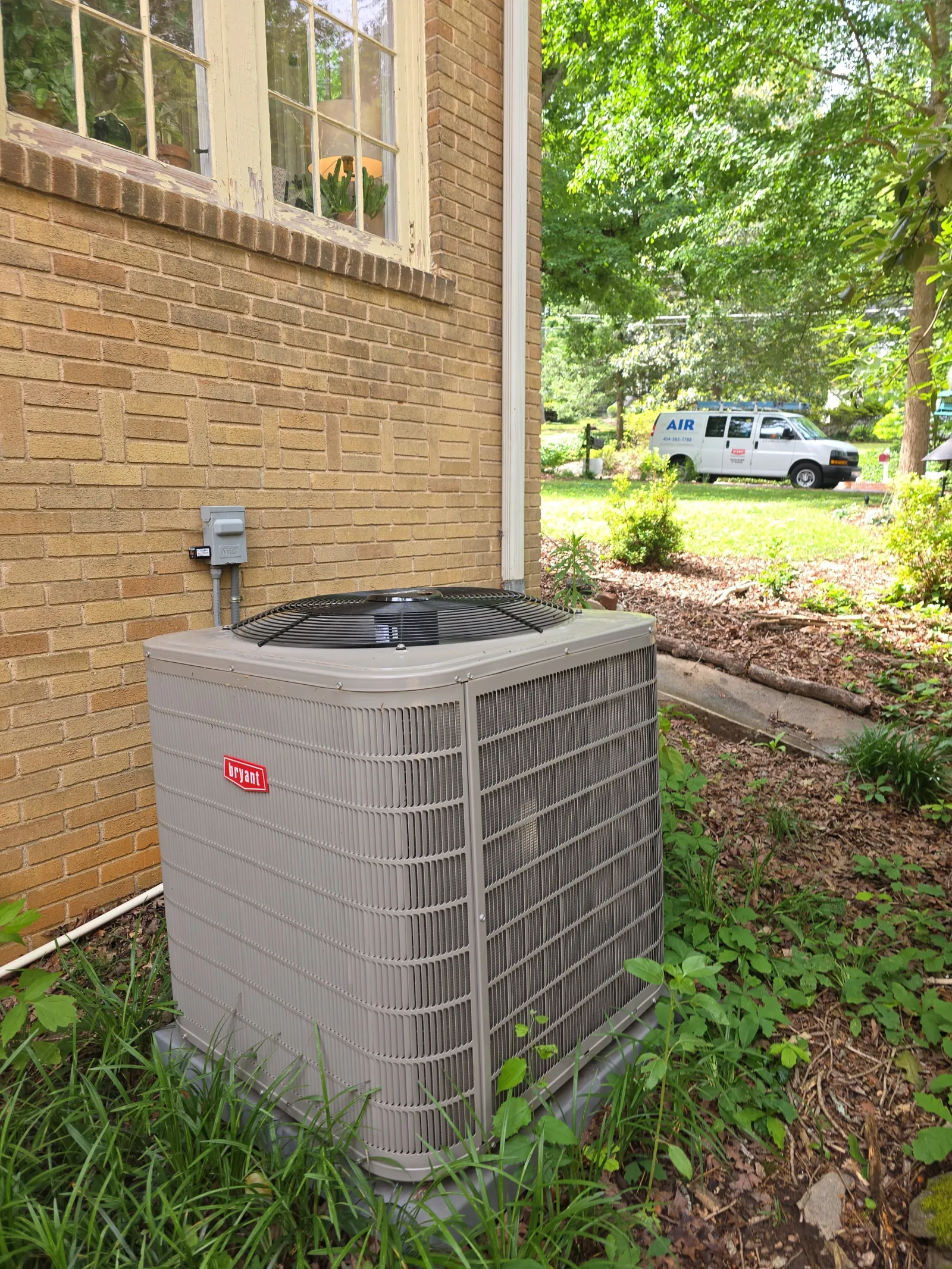 Atlanta HVAC Residential Repair by The Air Company of GA.  Bryant HVAC outdoor air conditioning unit installed next to a brick house with greenery and service van in background