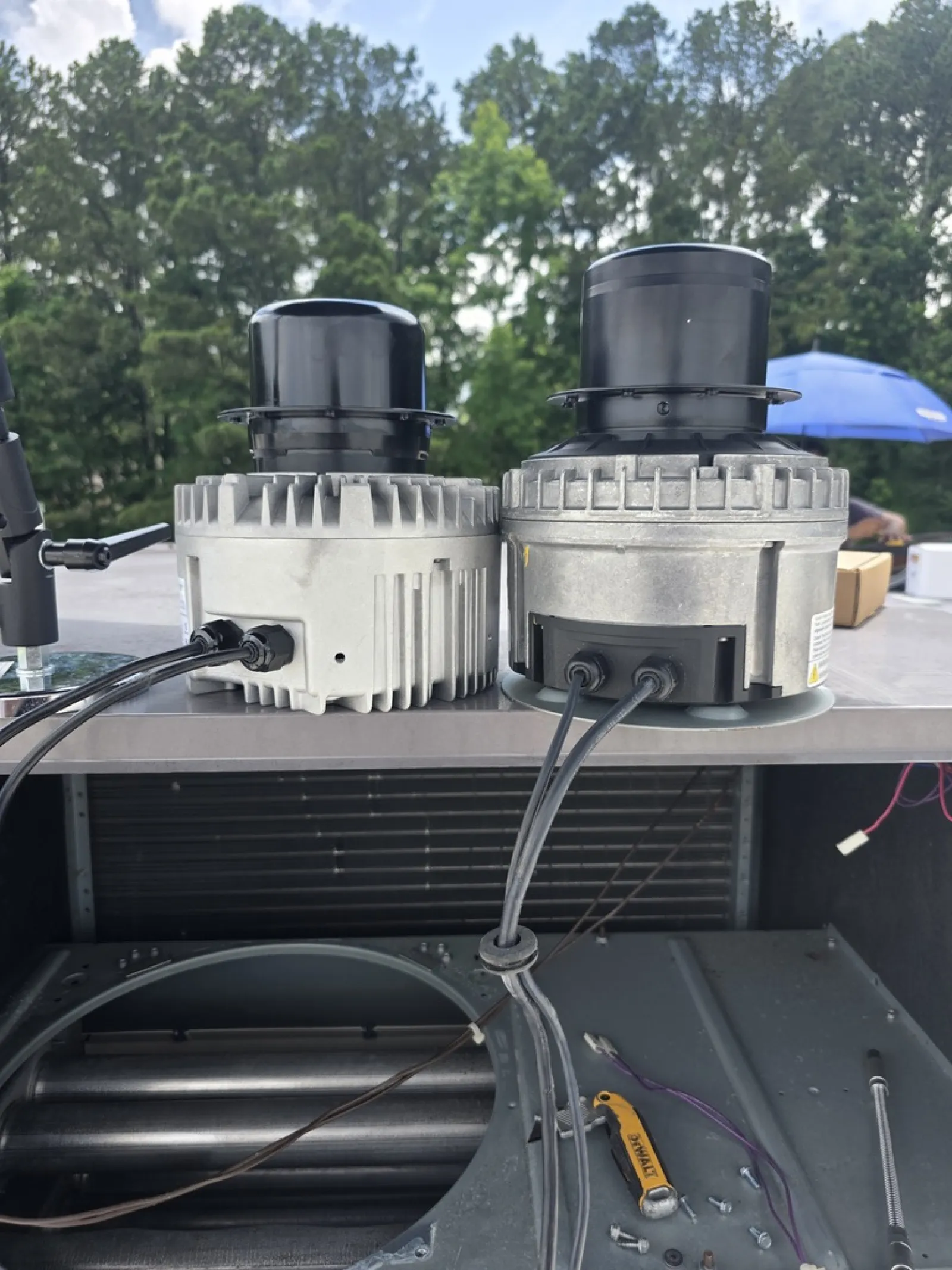 Two HVAC blower motors side by side on a metal surface with tools and screws nearby outdoors.