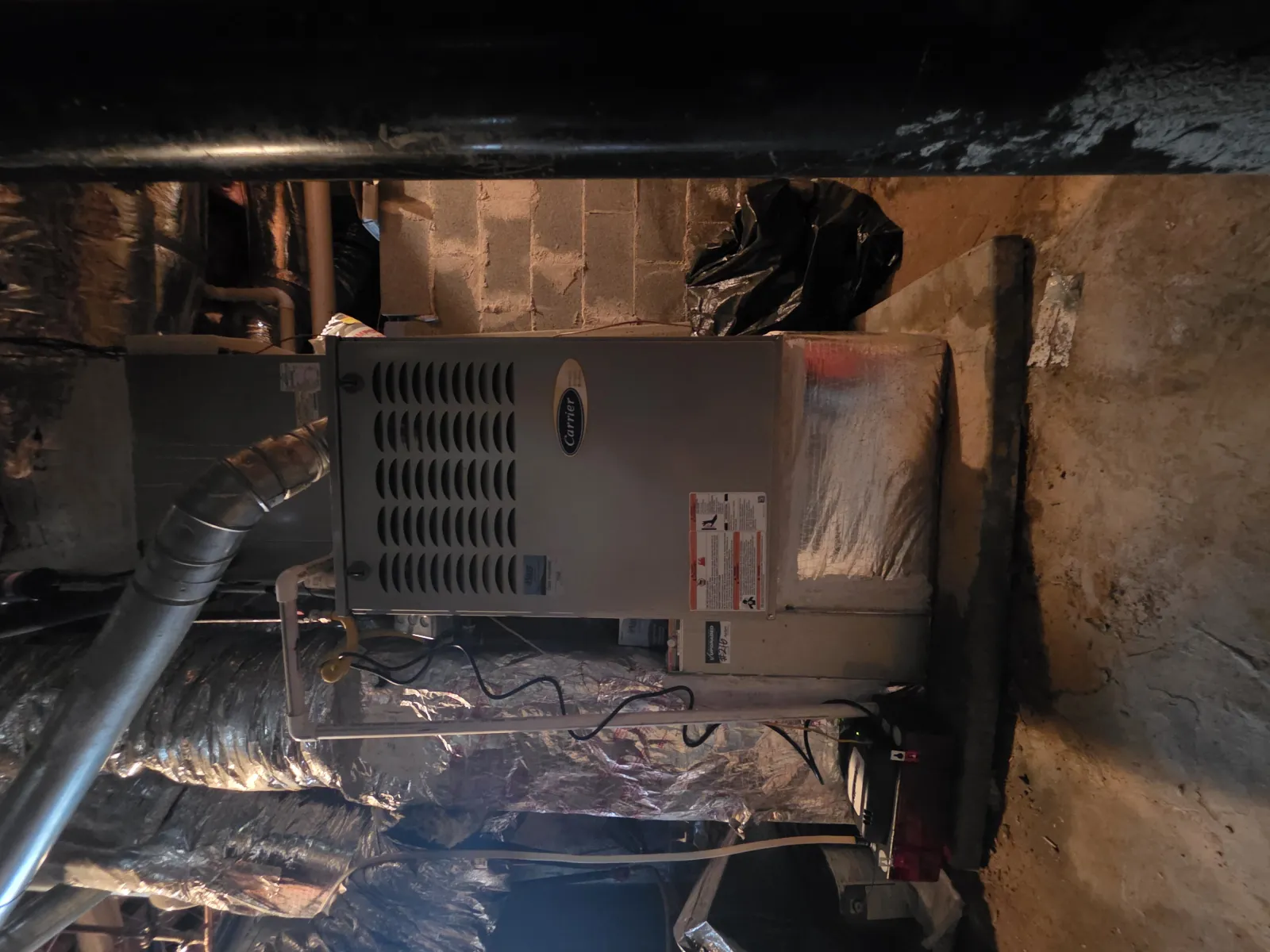 Furnace system with ductwork and insulated pipes in a basement with concrete block walls and floor.