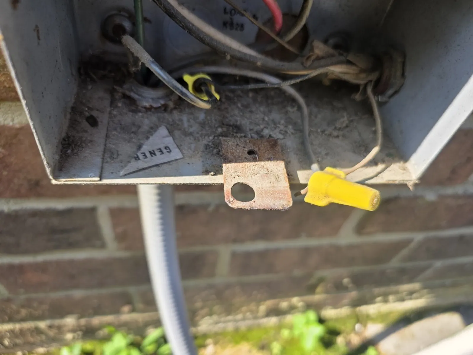 Close-up of an open outdoor electrical junction box with wires, wire connectors, and rusted metal components.