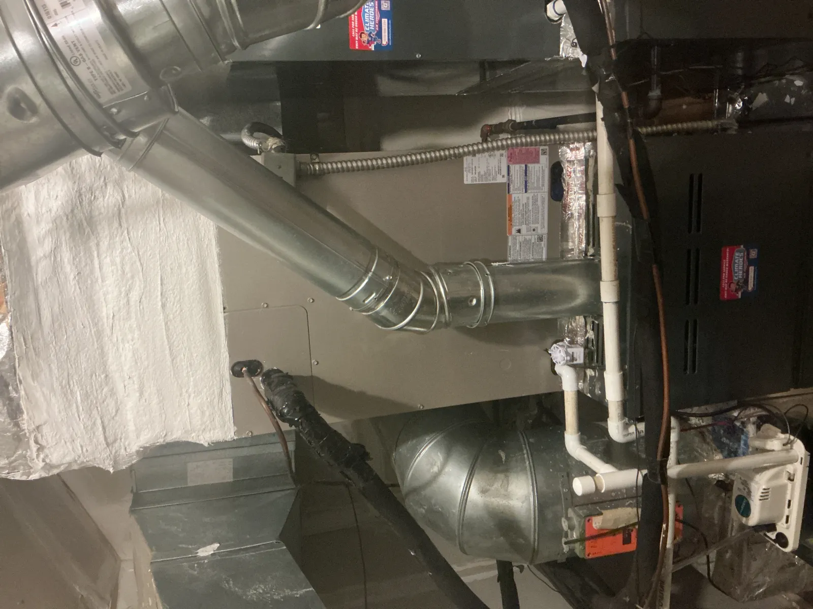 Industrial furnace and ductwork system in a utility basement with metal vents and pipes.