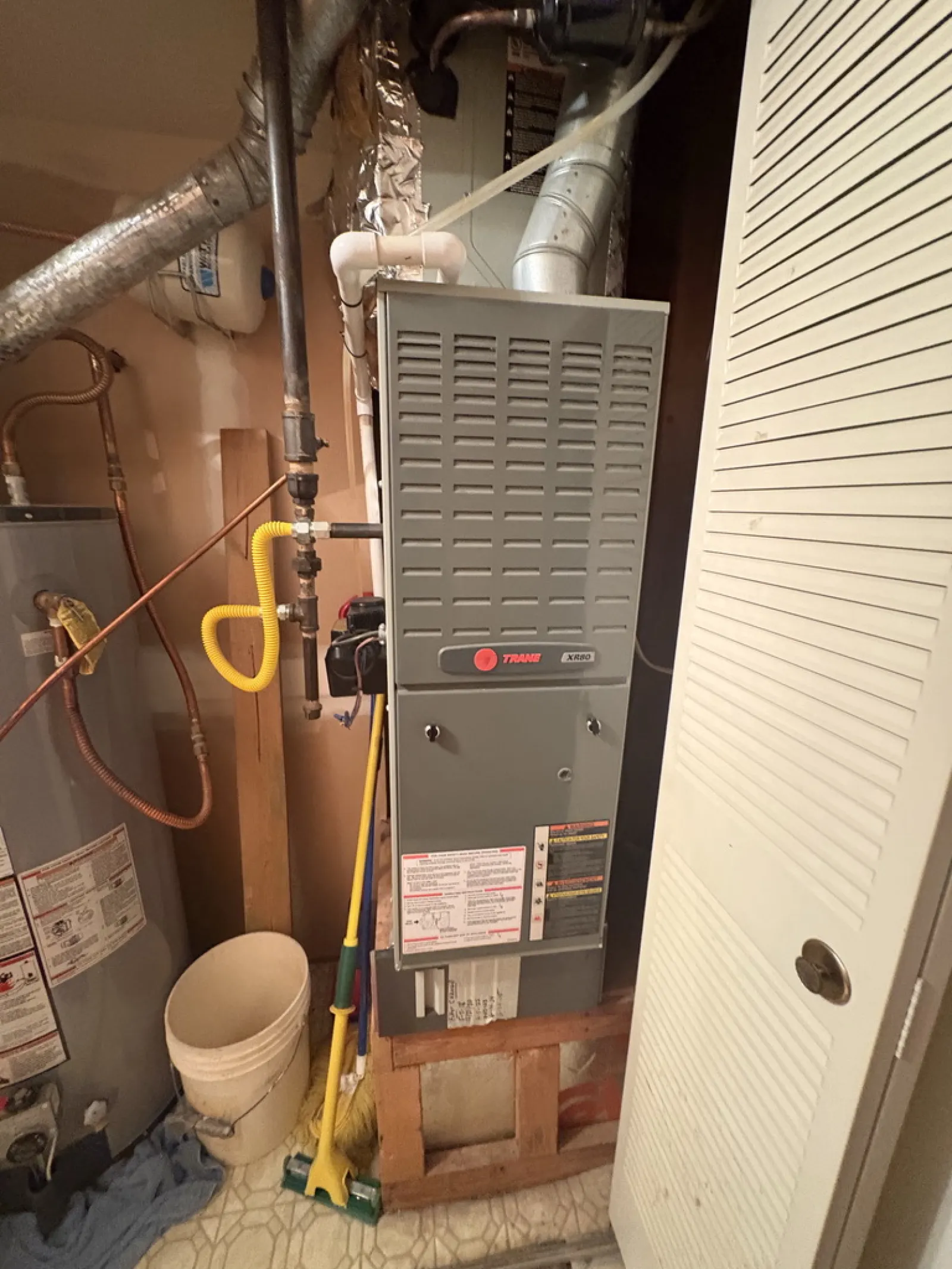 Trane XR80 furnace installed in a utility room next to a water heater and cleaning tools under soft lighting.