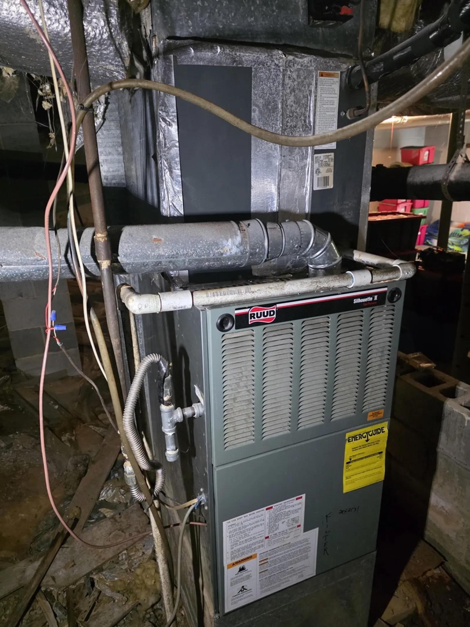 Ruud furnace unit with attached ductwork and piping in a basement setting with wiring visible.