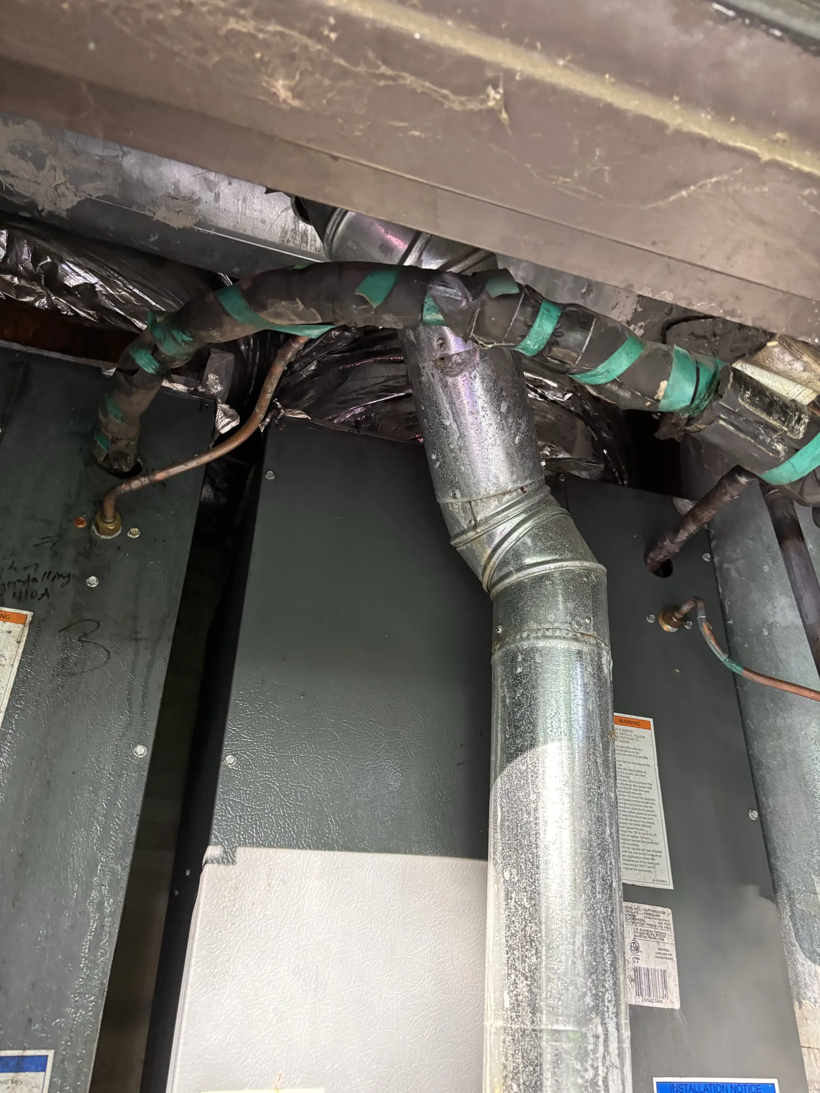 Metal ductwork and insulated pipes connected to a large furnace unit in a utility area.