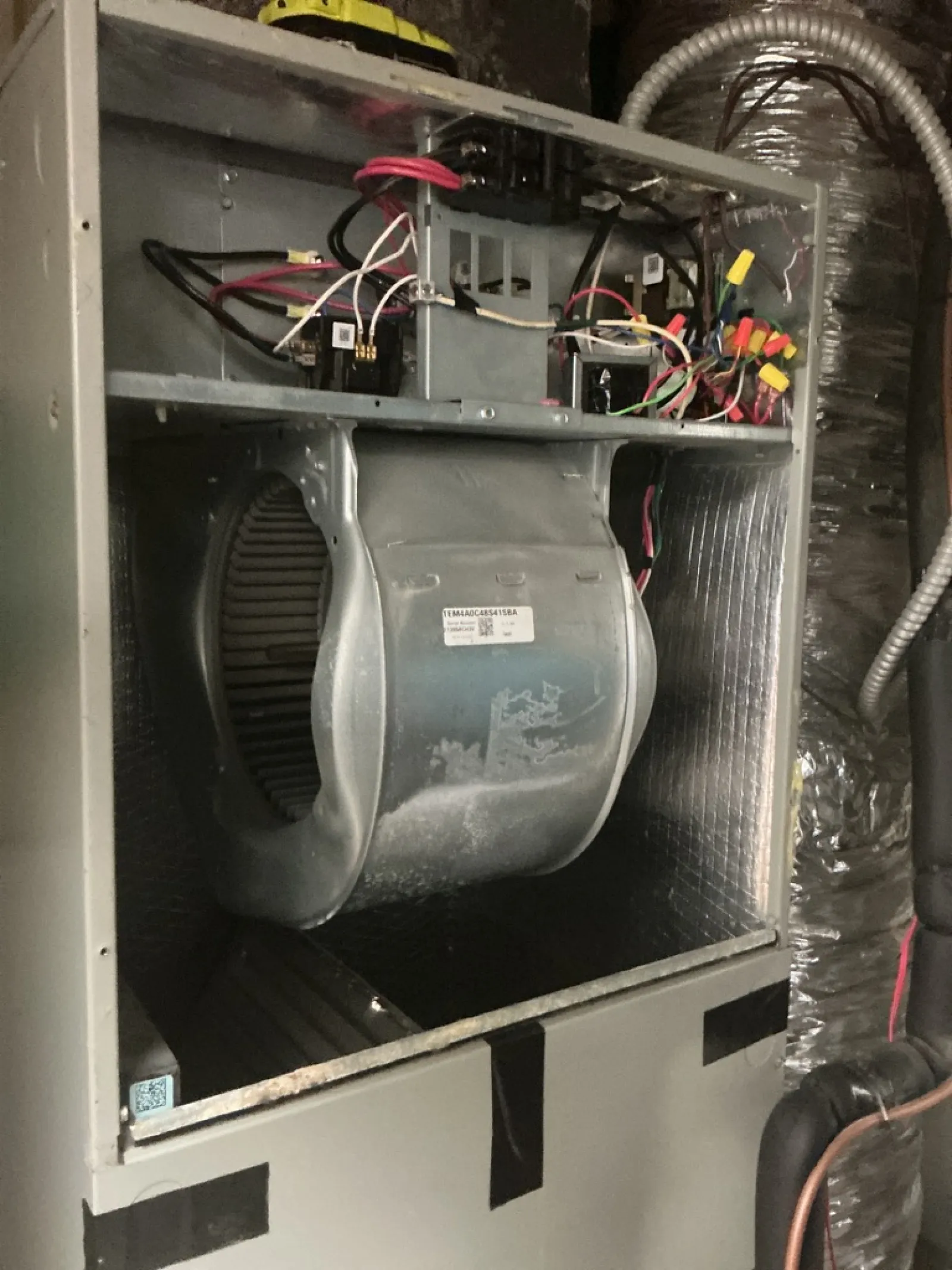 Interior of HVAC unit showing blower wheel, wiring, and ventilation components inside metal casing.