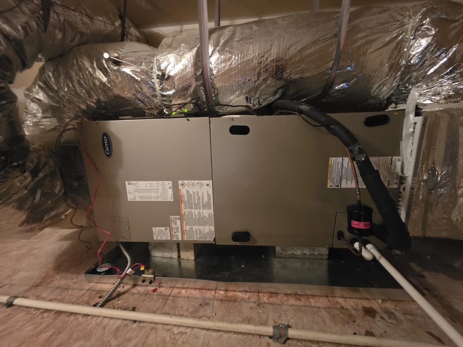 Carrier HVAC unit installed in a basement with insulated ductwork and connected pipes and wires.