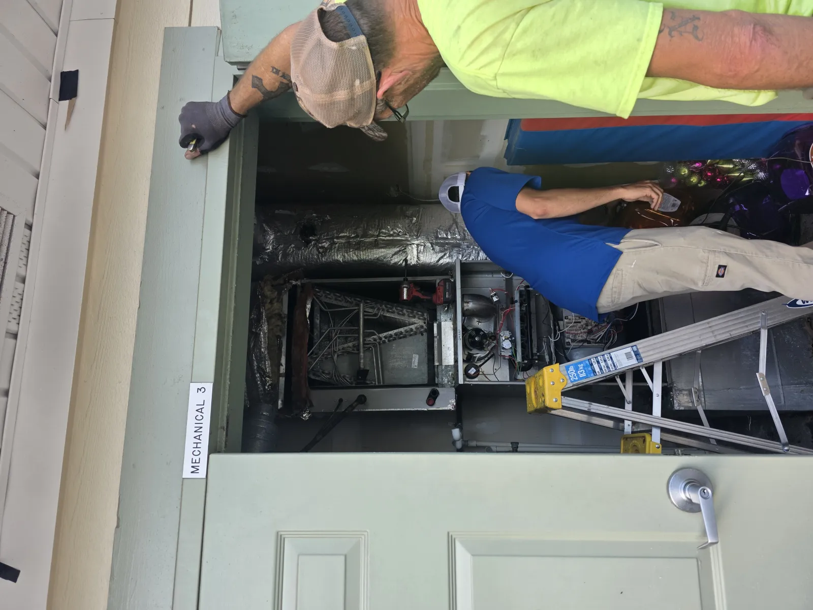 Two technicians inspect HVAC equipment in a mechanical room labeled Mechanical 3 with a ladder nearby.