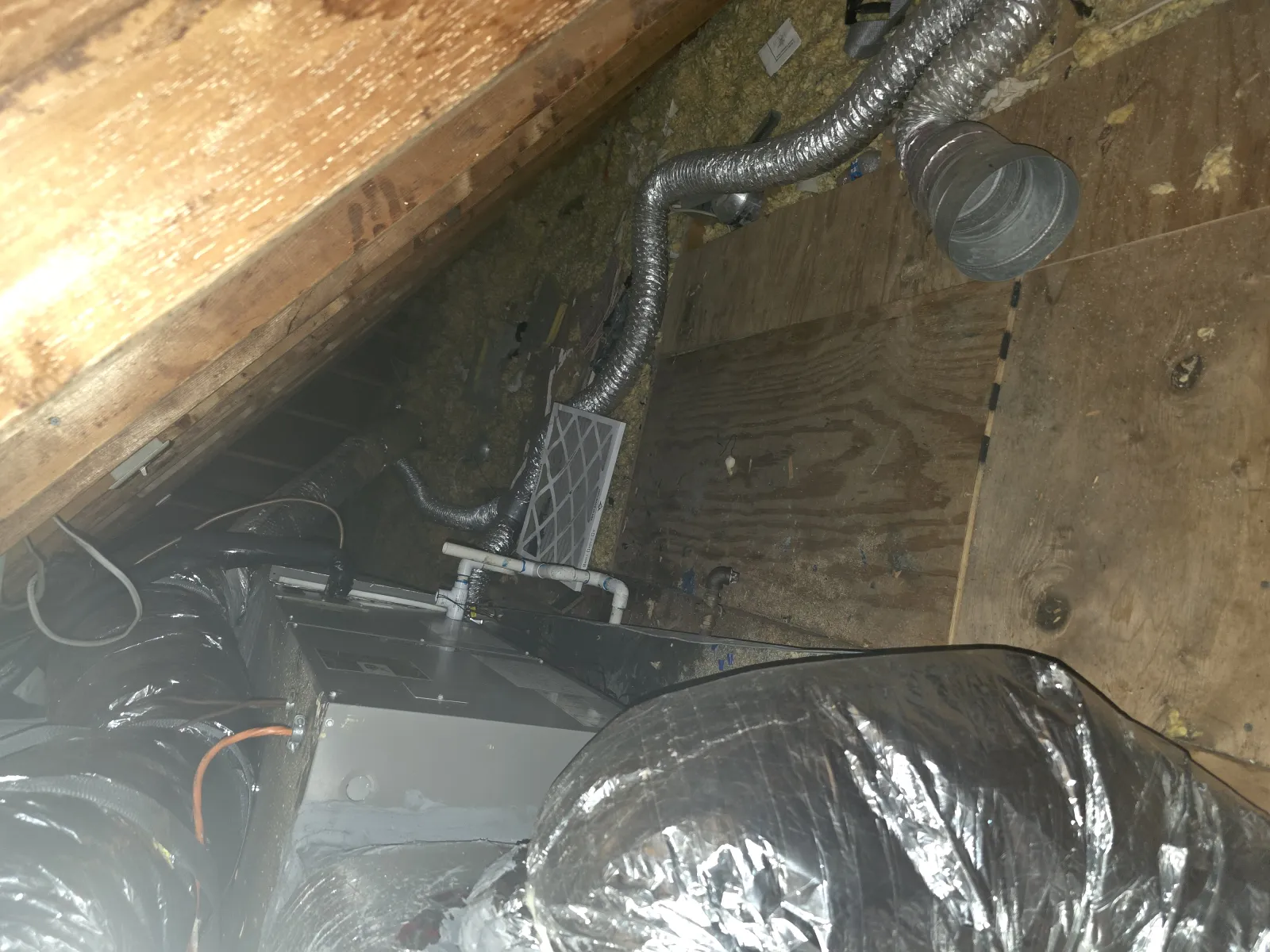 HVAC unit with ducts installed in an attic with wooden beams and insulation
