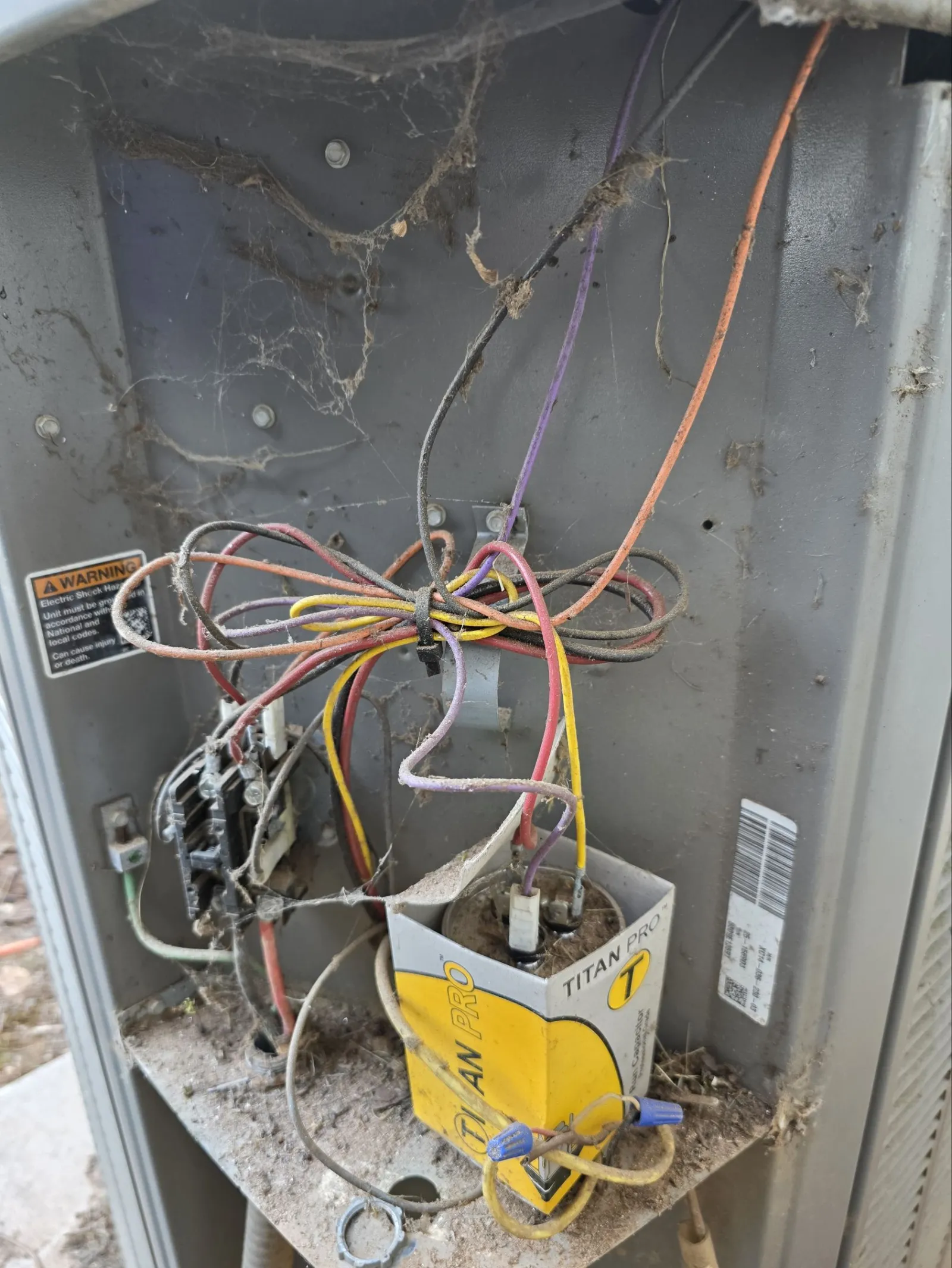 AC Cooling Repair in Sandy Springs 30328 by The Air Company of GA. Dusty and cobweb-covered electrical wiring and a Titan Pro capacitor inside a damaged HVAC unit.