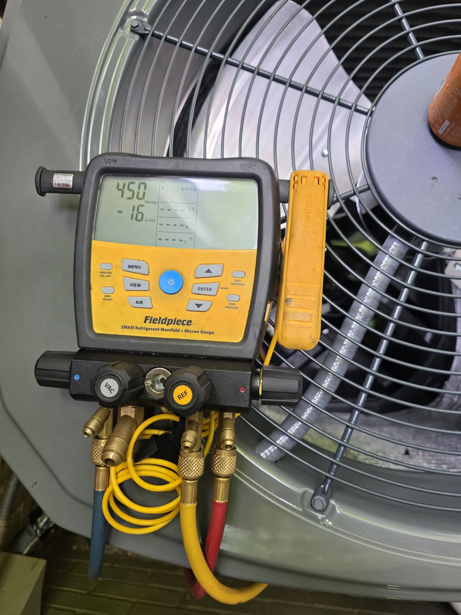 Fieldpiece SMAN refrigerant manifold gauge connected to HVAC unit measuring pressure and vacuum.