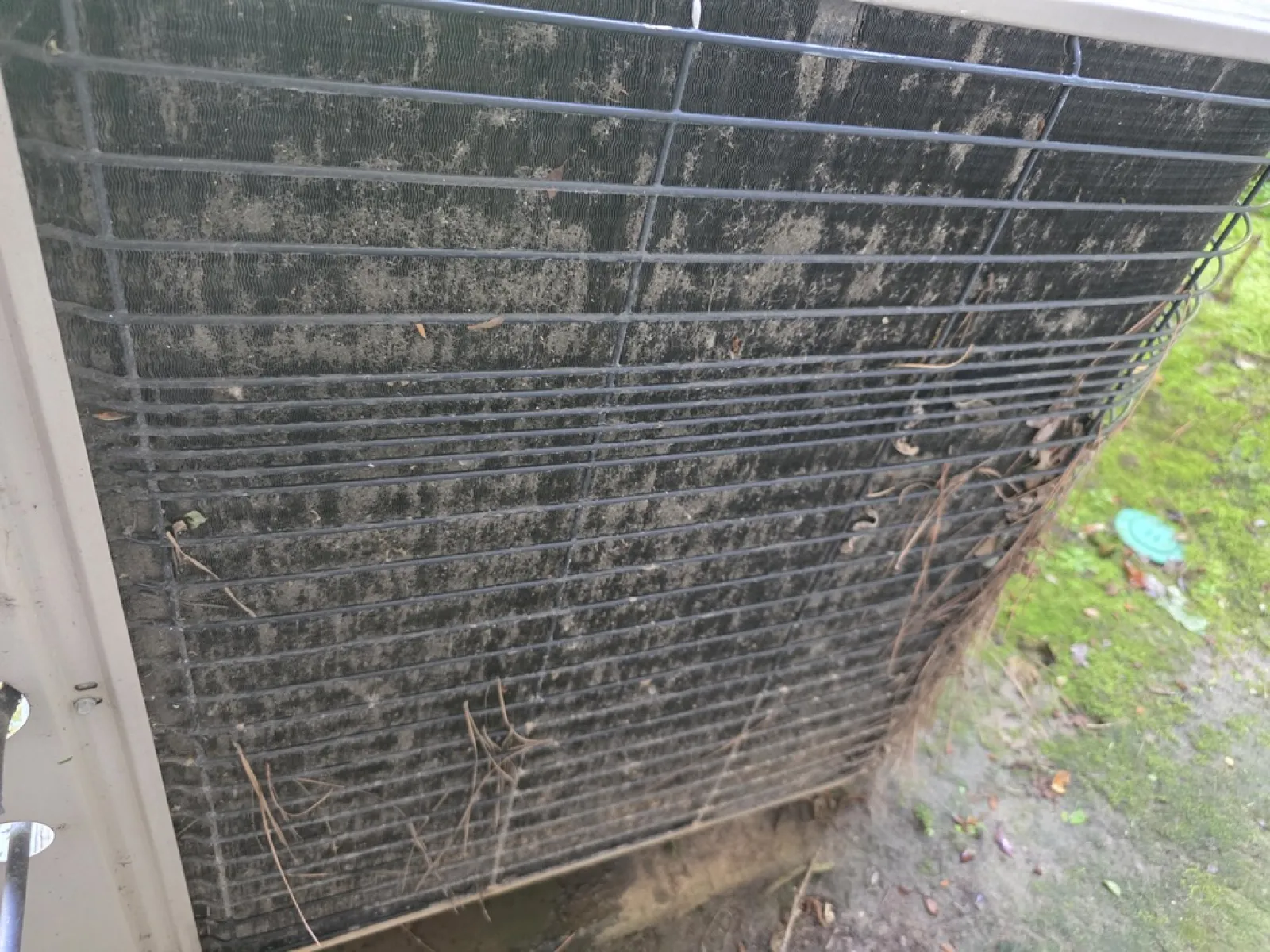 Dirty and clogged outdoor air conditioner condenser coil covered with dirt, debris, and dried leaves.