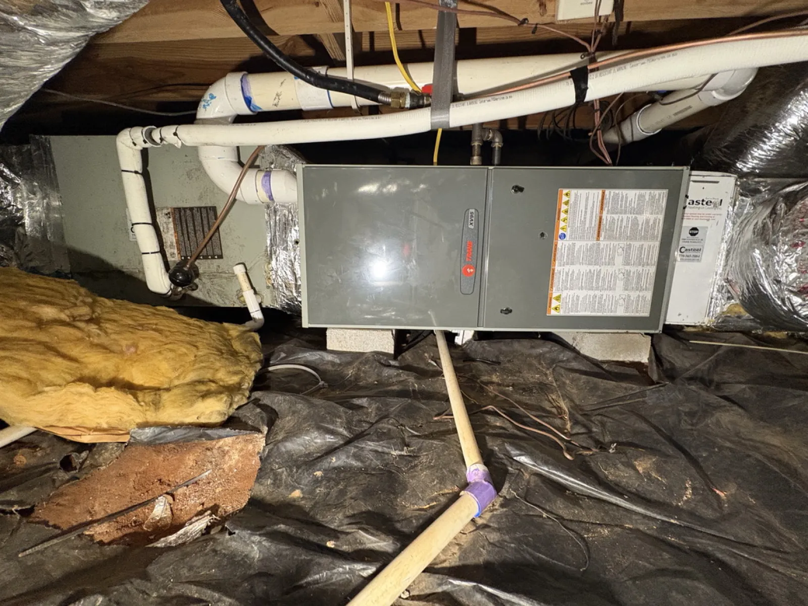 HVAC furnace and ductwork installed in a basement crawl space with insulation and pipes visible
